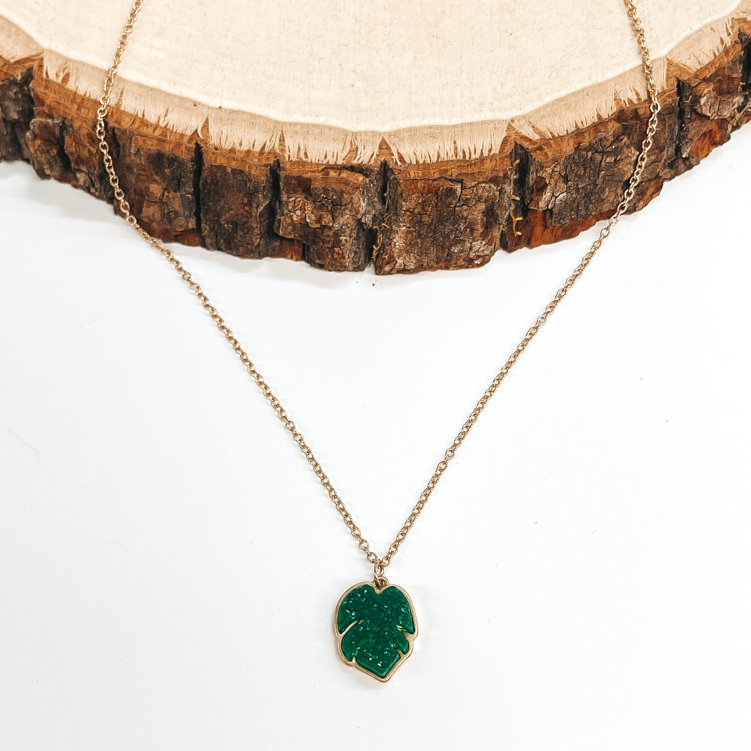 Gold necklace with a palm leaf druzy pendant in  green. Taken on a white background and a piece of  wood. 