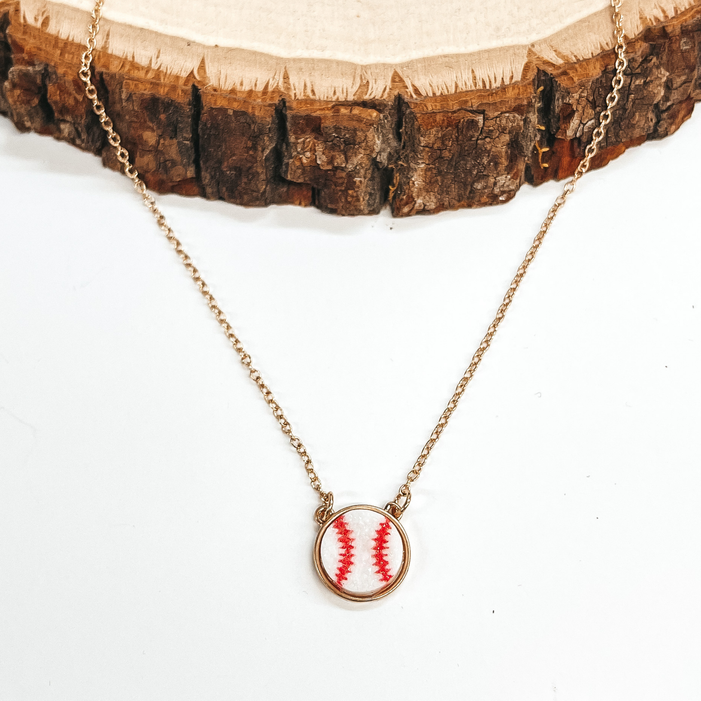 Gold necklace with a baseball druzy pendant in white  and red. Taken on a white background and a piece of  wood. 