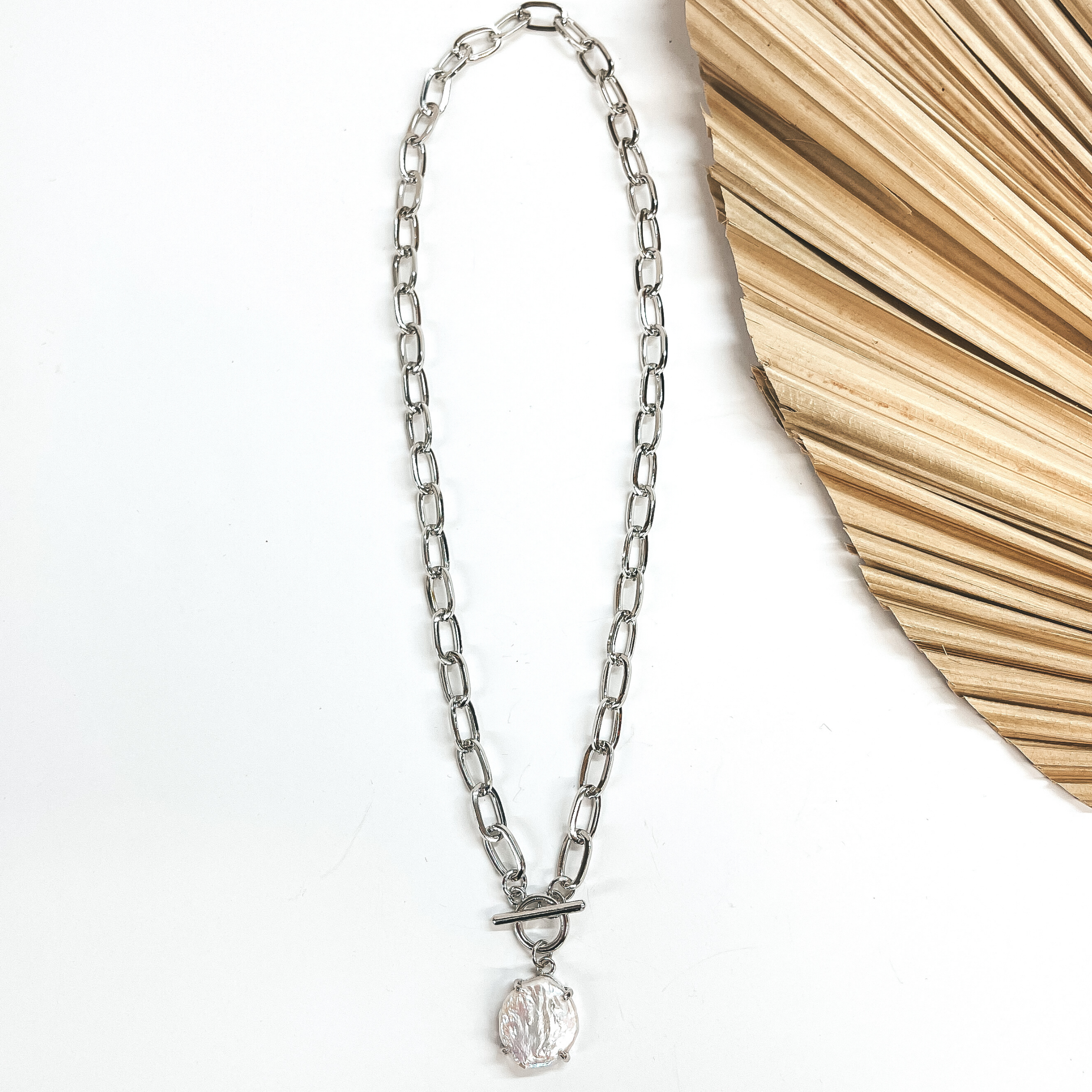 Silver thick chain with a toggle clasp and  freshwater pearl pendant. Taken on a white background and a dried up palm leaf in the side as decor.