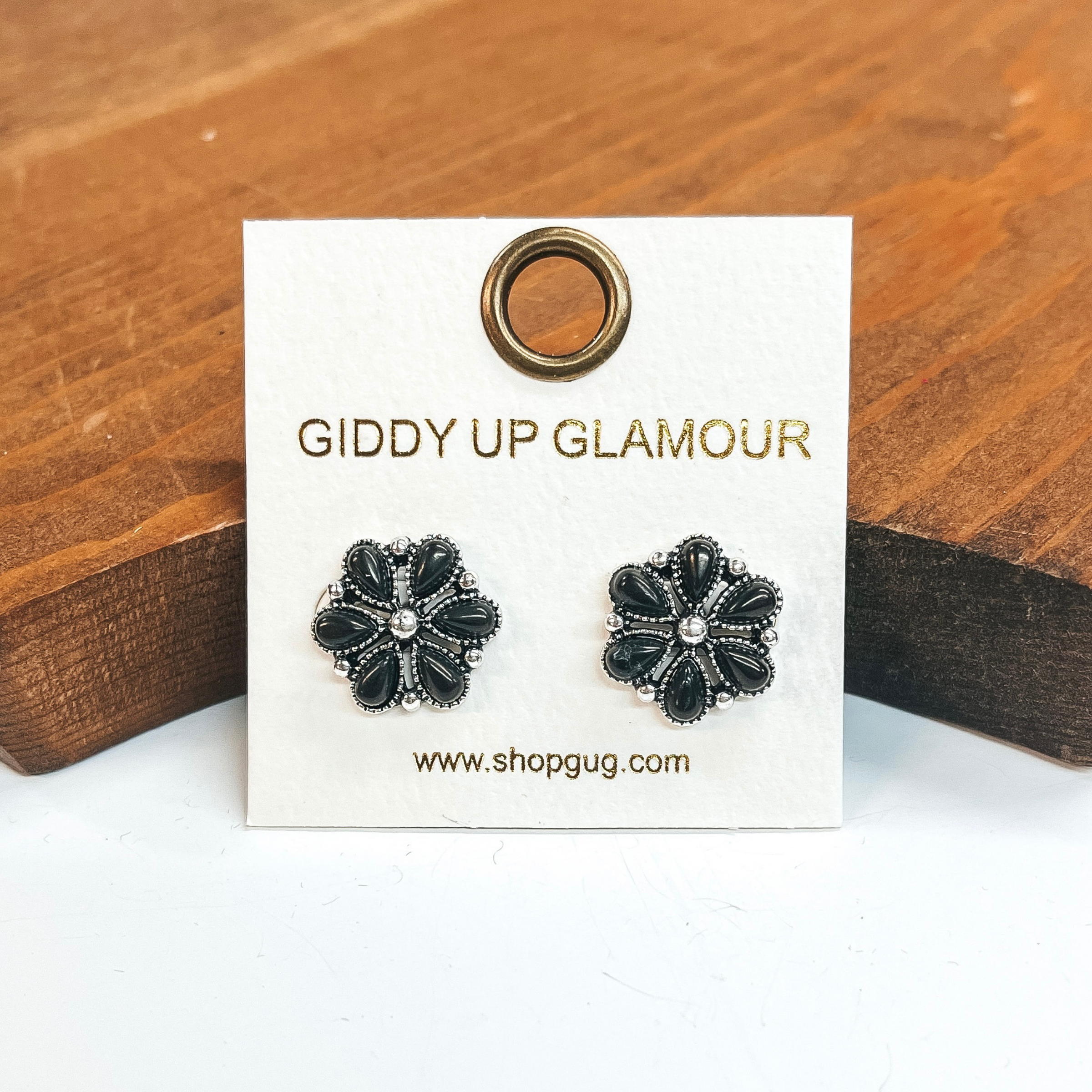 Silver flower earrings that include black stones.  These earrings are taken on a white background and leaned up against a brown block.
