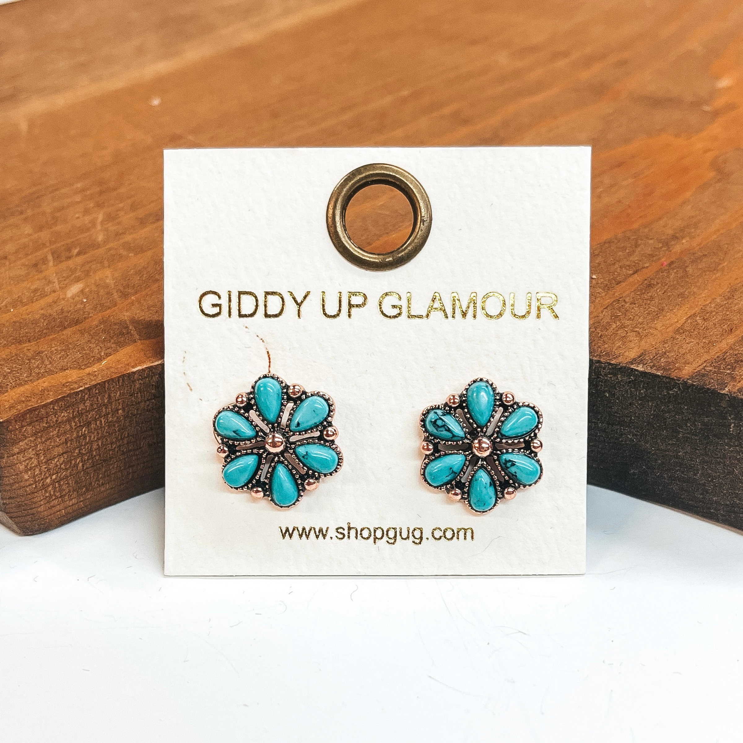 Copper flower earrings that include turquoise stones.  These earrings are taken on a white background and leaned up against a brown block.