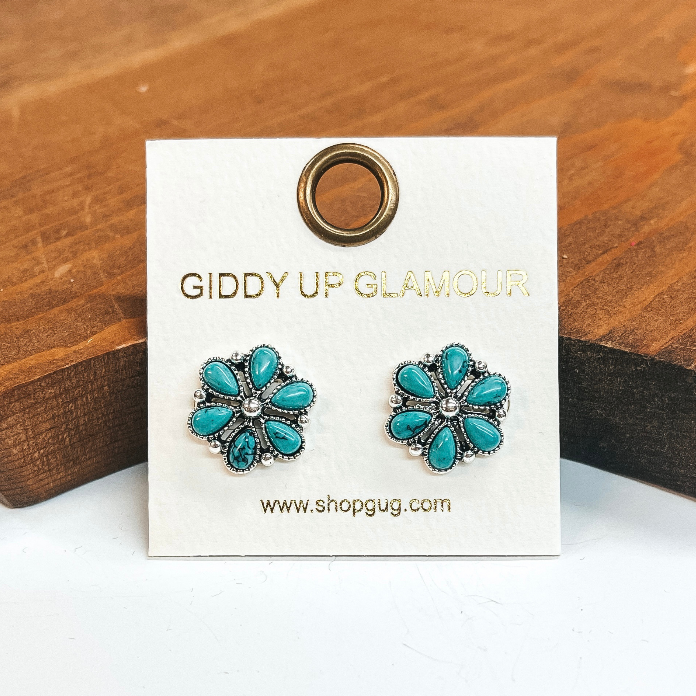 Silver flower earrings that include turquoise stones.  These earrings are taken on a white background and leaned up against a brown block.