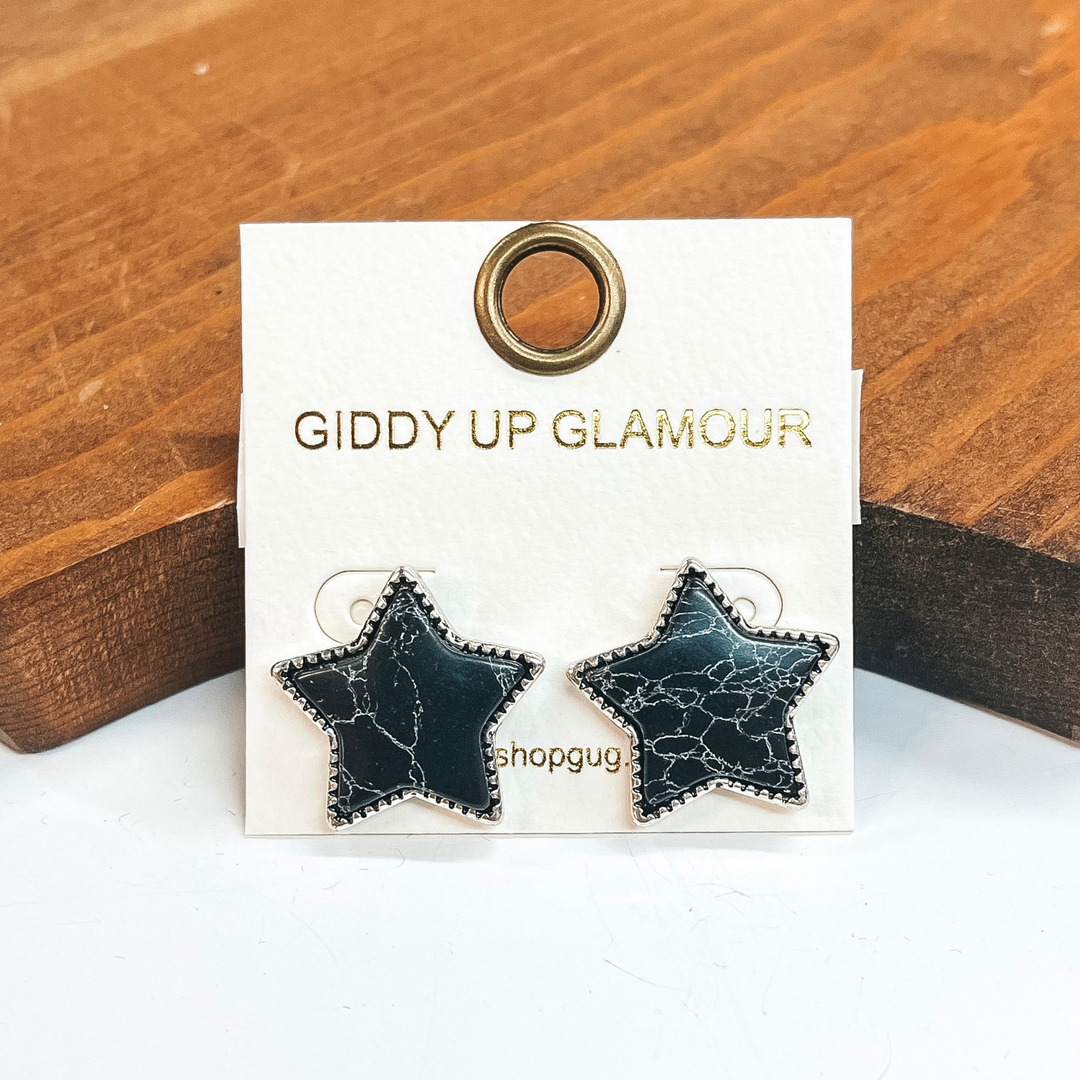 Silver star post earrings that include a black stone  with white lines.  These earrings are taken on a white background and leaned up against a brown block.