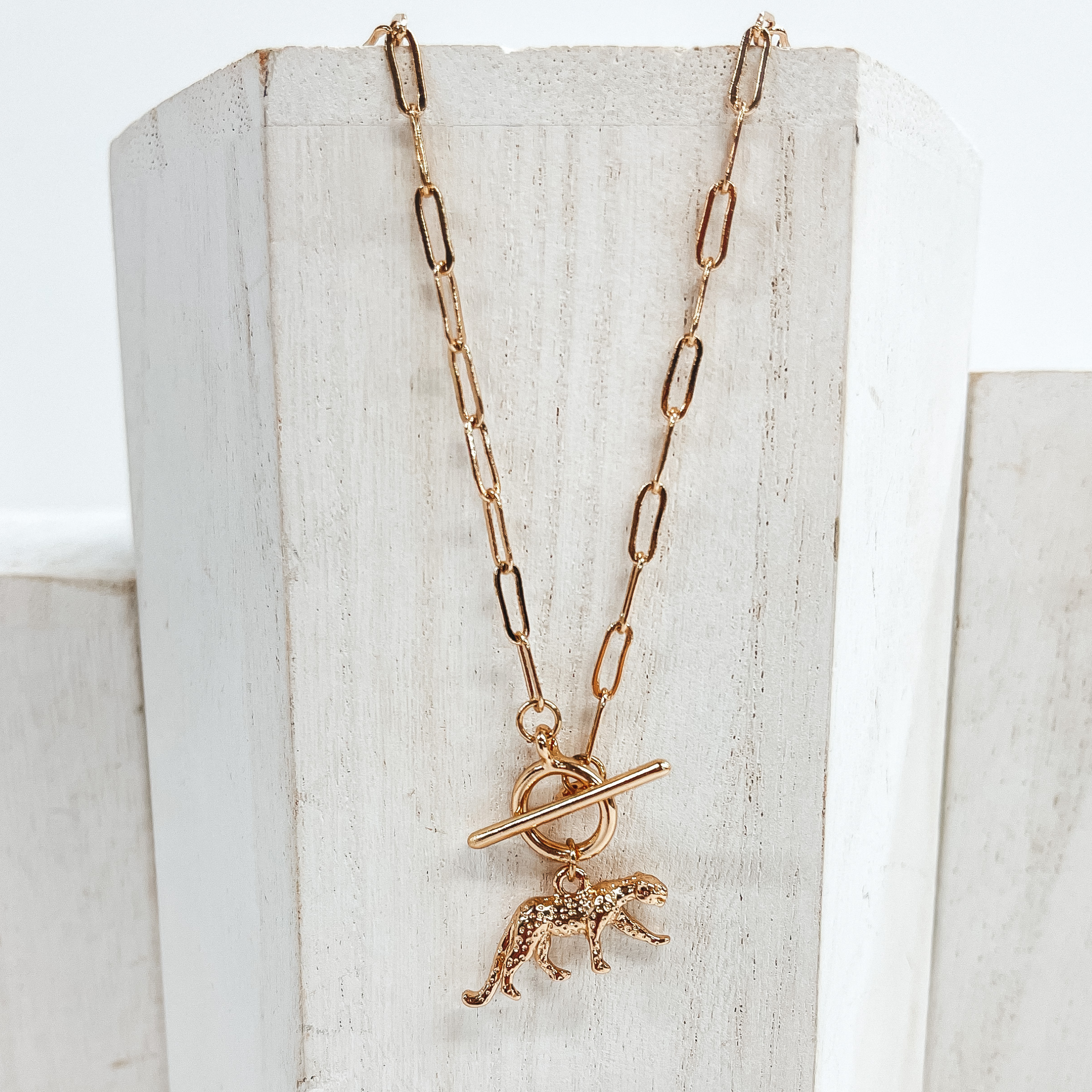 This is a gold chain necklace with a front  toggle clasp and a jaguar pendant.  This necklace is pictured laying on a  white block and on a white background