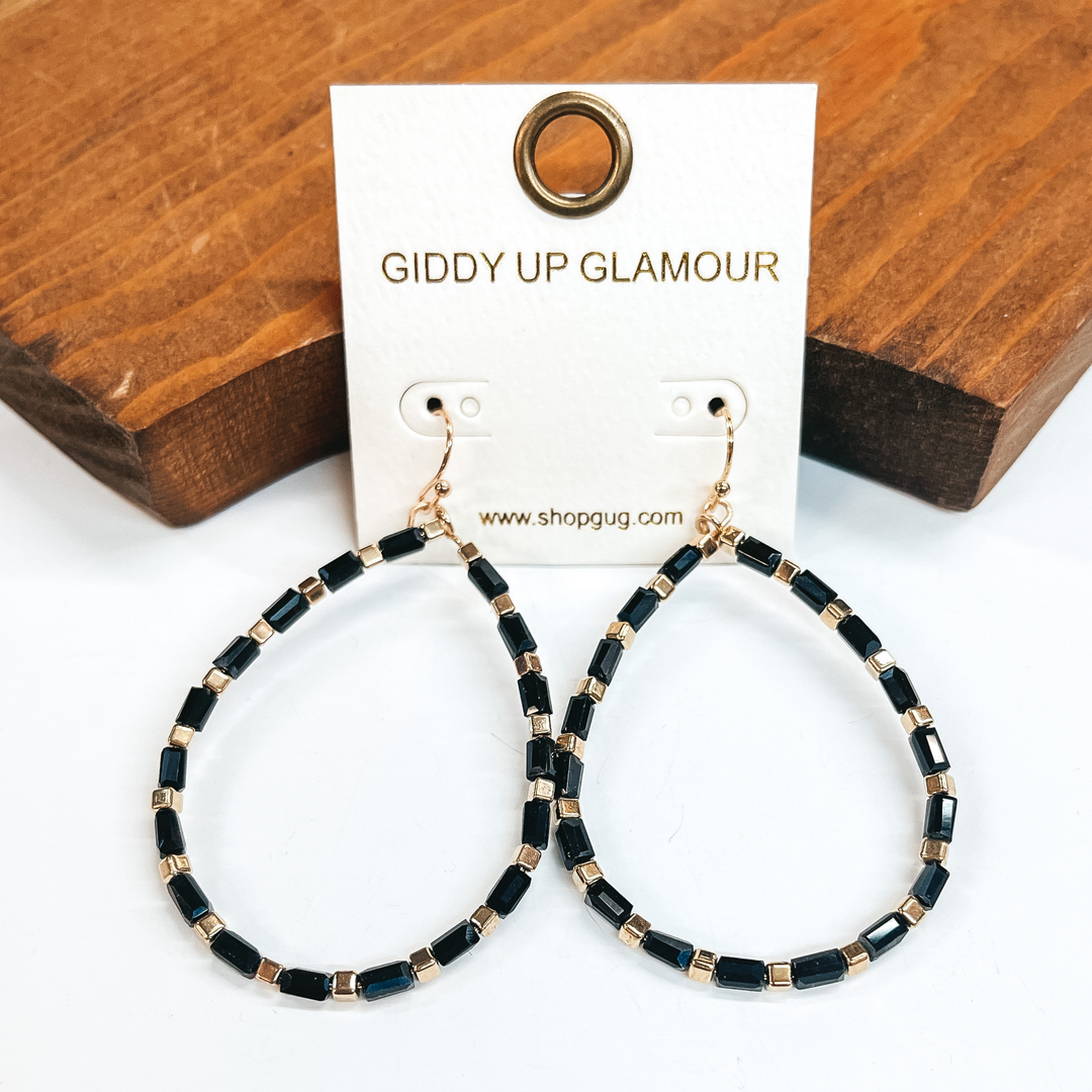 Gold fish hook teardrop earrings with gold square  beads and long black crystal beads. Taken on a  white background and leaned up against a brown block.