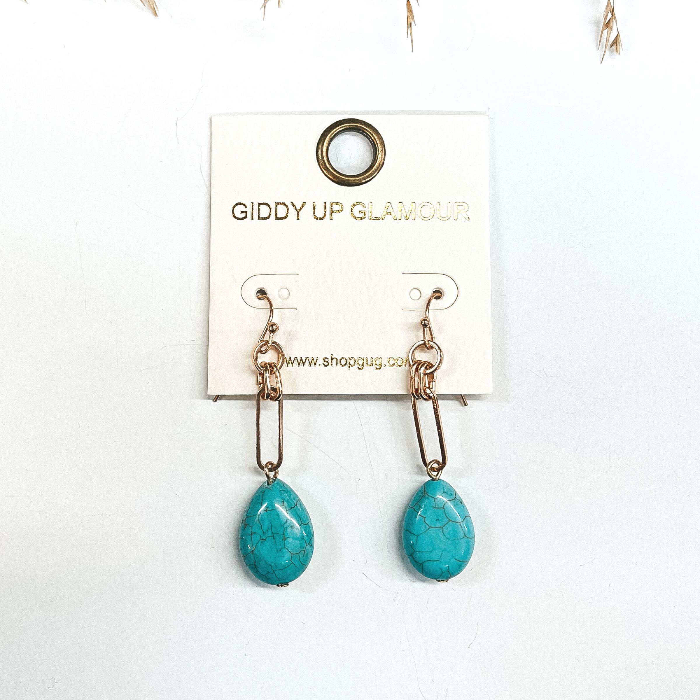 Gold chain earrings with a faux turquoise stone drop. Taken on a white background with a brown plant in the  back as decor.