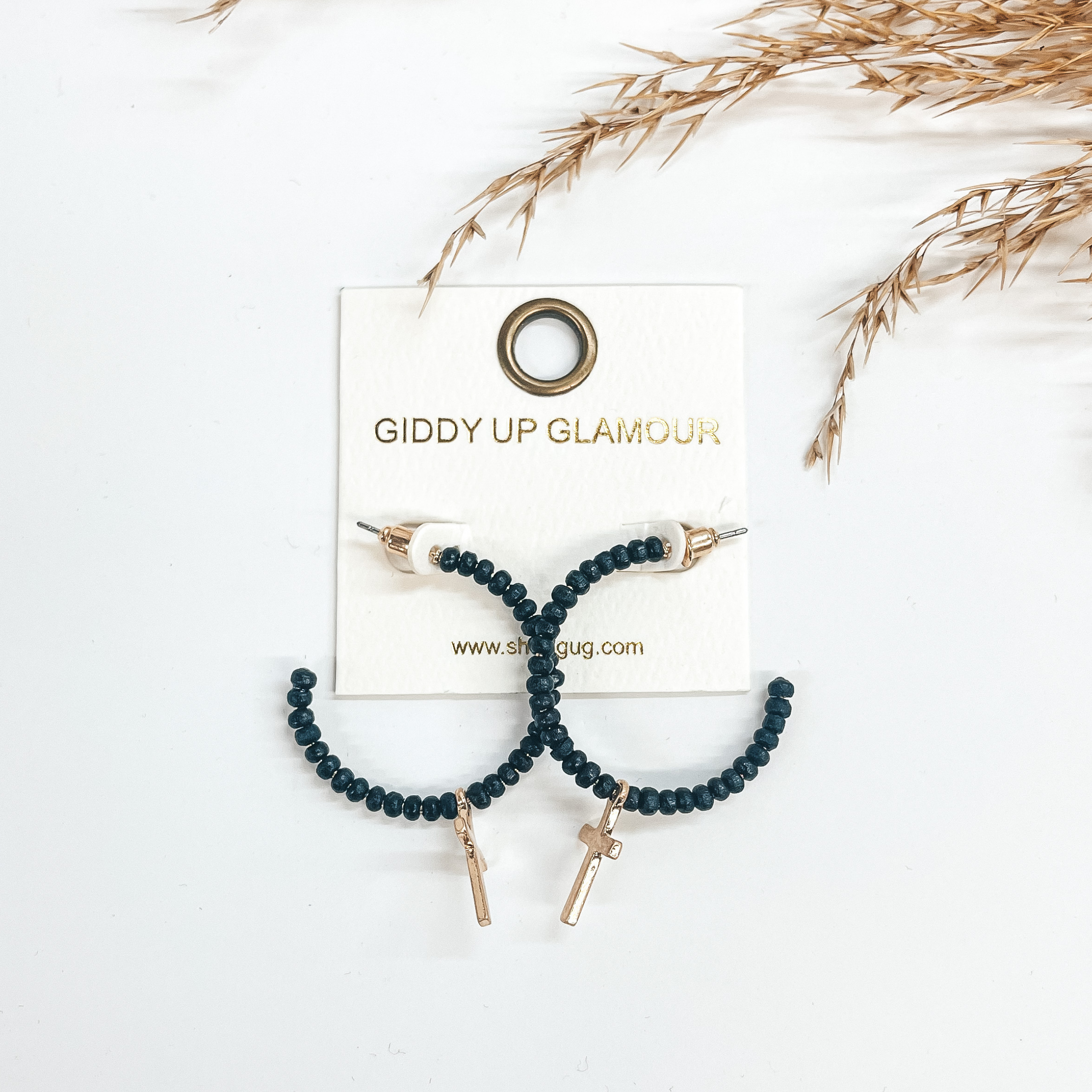 Open ended hoops with black wooded beads all around  and a gold cross pendant. Taken on a white background  and a brown plant in the back as decor. 
