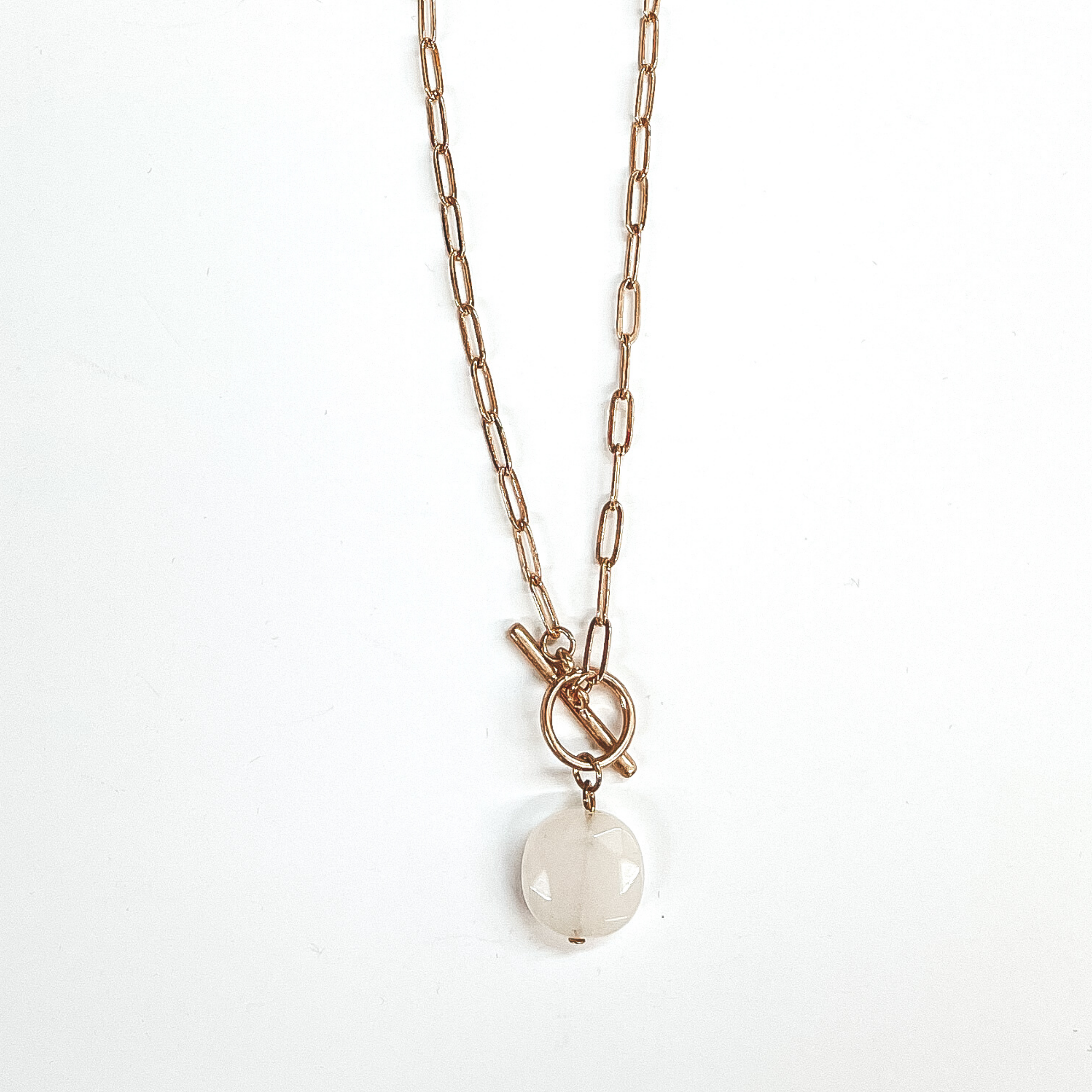 Gold paperclip chain necklace with toggle clasp and  natural stone circle pendant in ivory. Taken on  a white background.