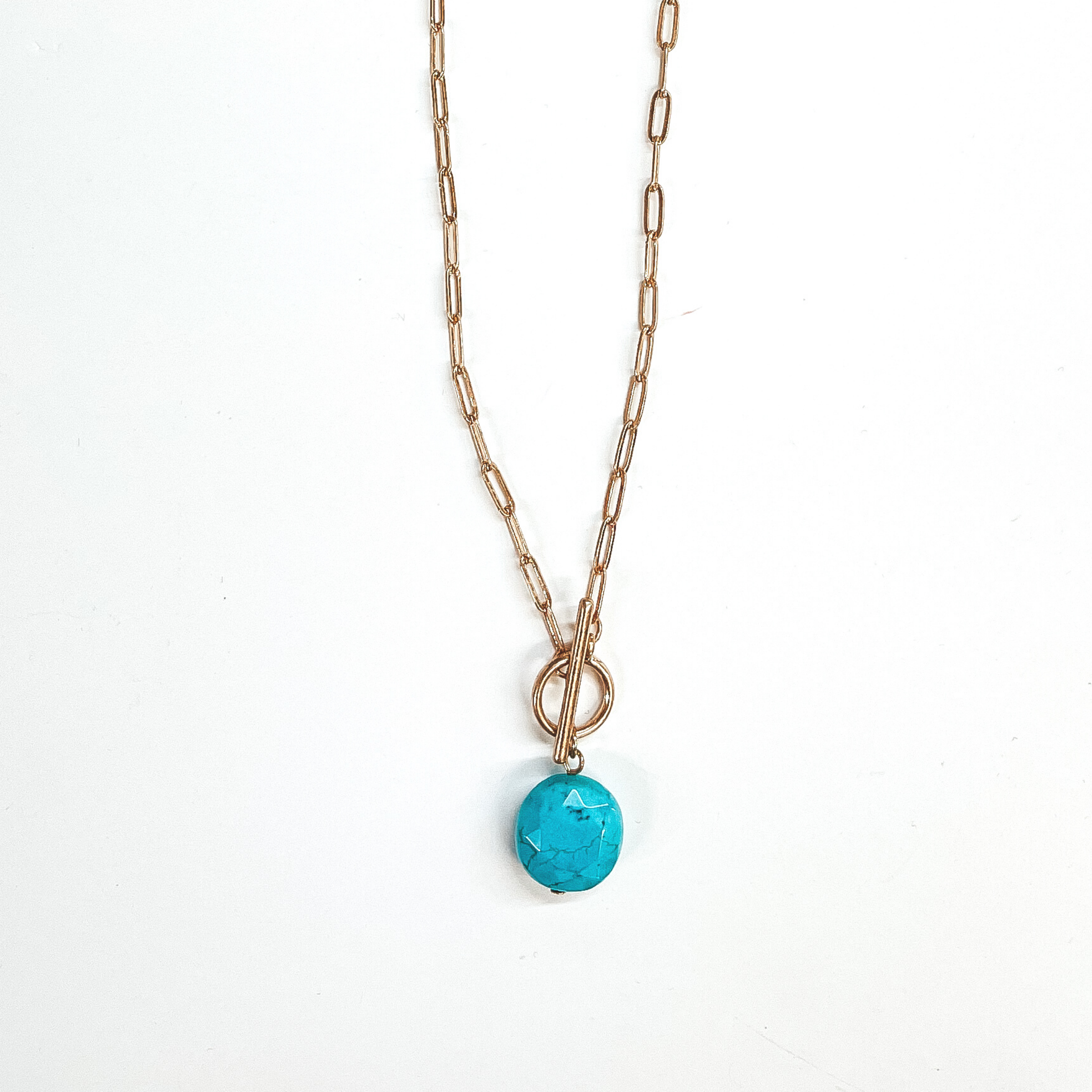 Gold paperclip chain necklace with toggle clasp and  natural stone circle pendant in turquoise. Taken on  a white background.