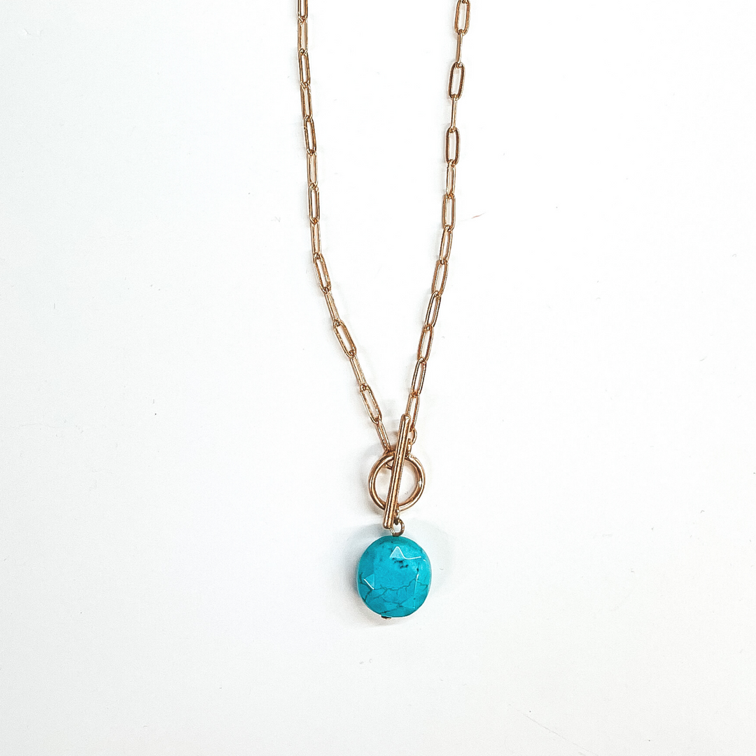 Gold paperclip chain necklace with toggle clasp and  natural stone circle pendant in turquoise. Taken on  a white background.