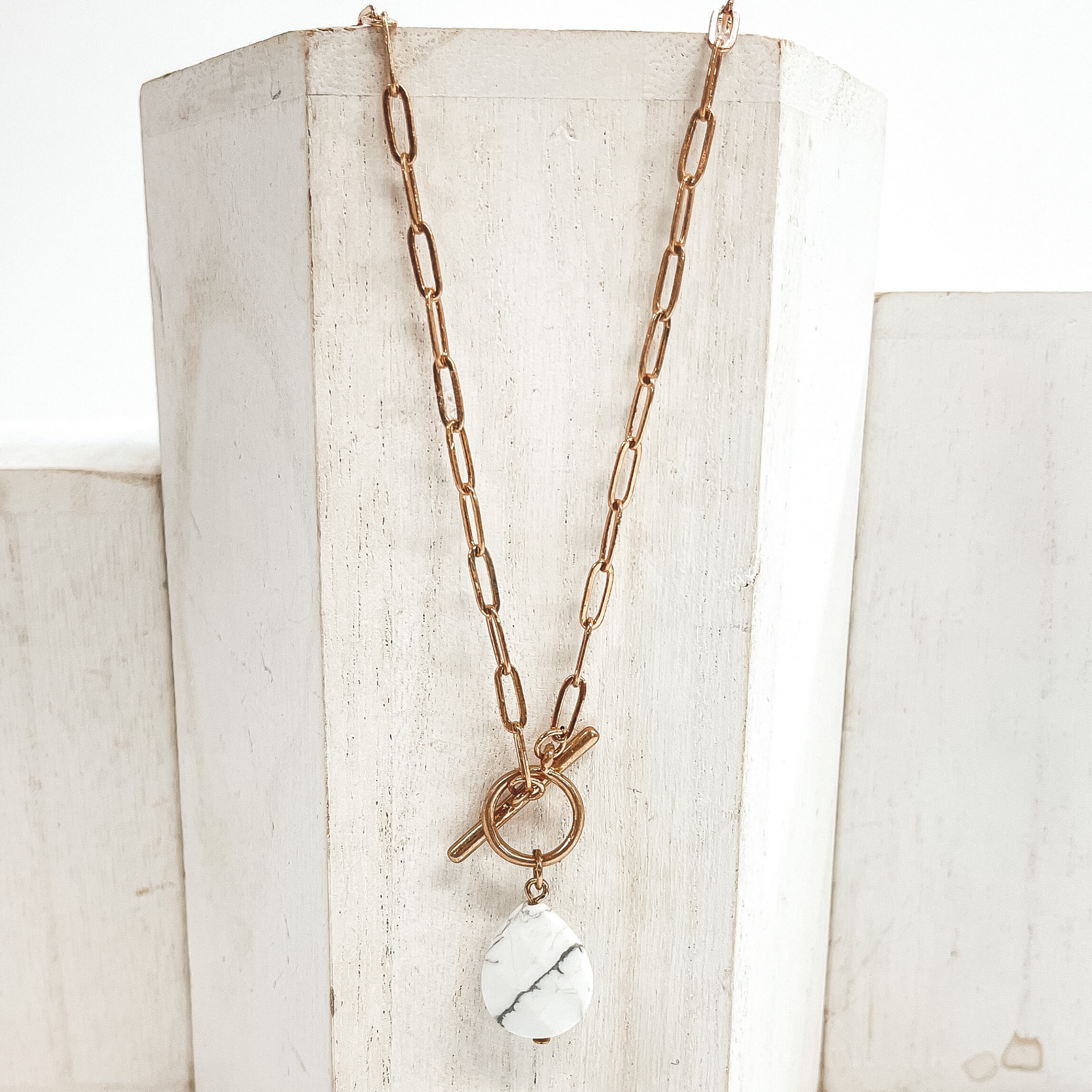 Gold paperclip chain necklace with toggle clasp and  natural stone teardrop pendant in white.  Taken on  a white block and white background.