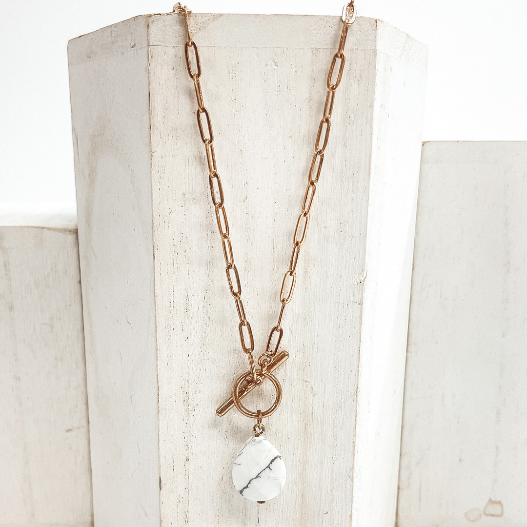 Gold paperclip chain necklace with toggle clasp and  natural stone teardrop pendant in white.  Taken on  a white block and white background.