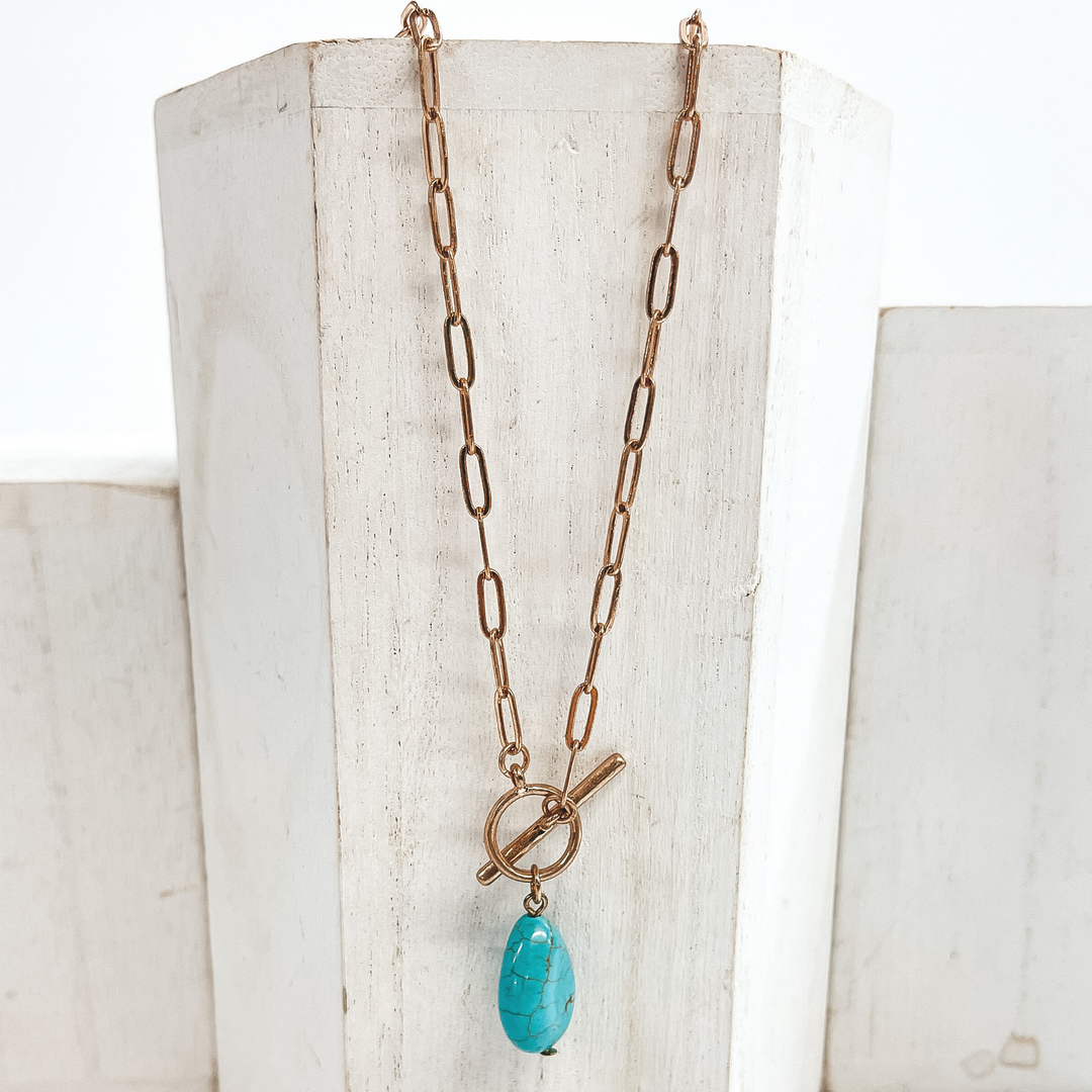 Gold paperclip chain necklace with toggle clasp and  natural stone teardrop pendant in turquoise.  Taken on  a white block and white background.