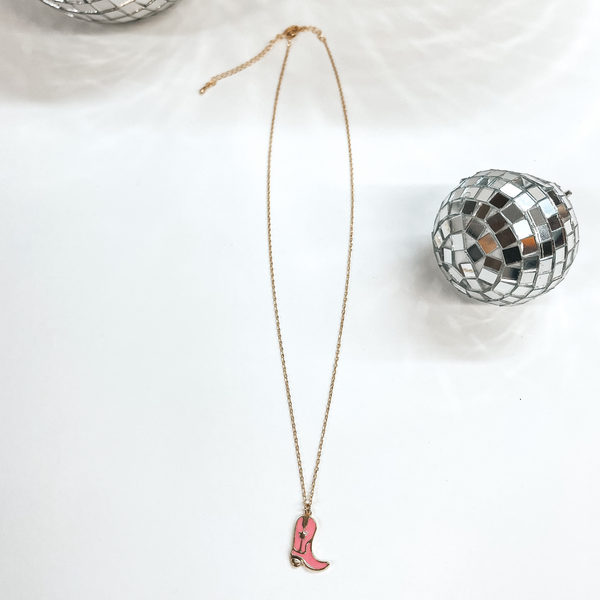 Small gold chain necklace with a pink boot pendant,  the boot pendant has a gold star in the center.  Taken on a white background with disco balls as decor.