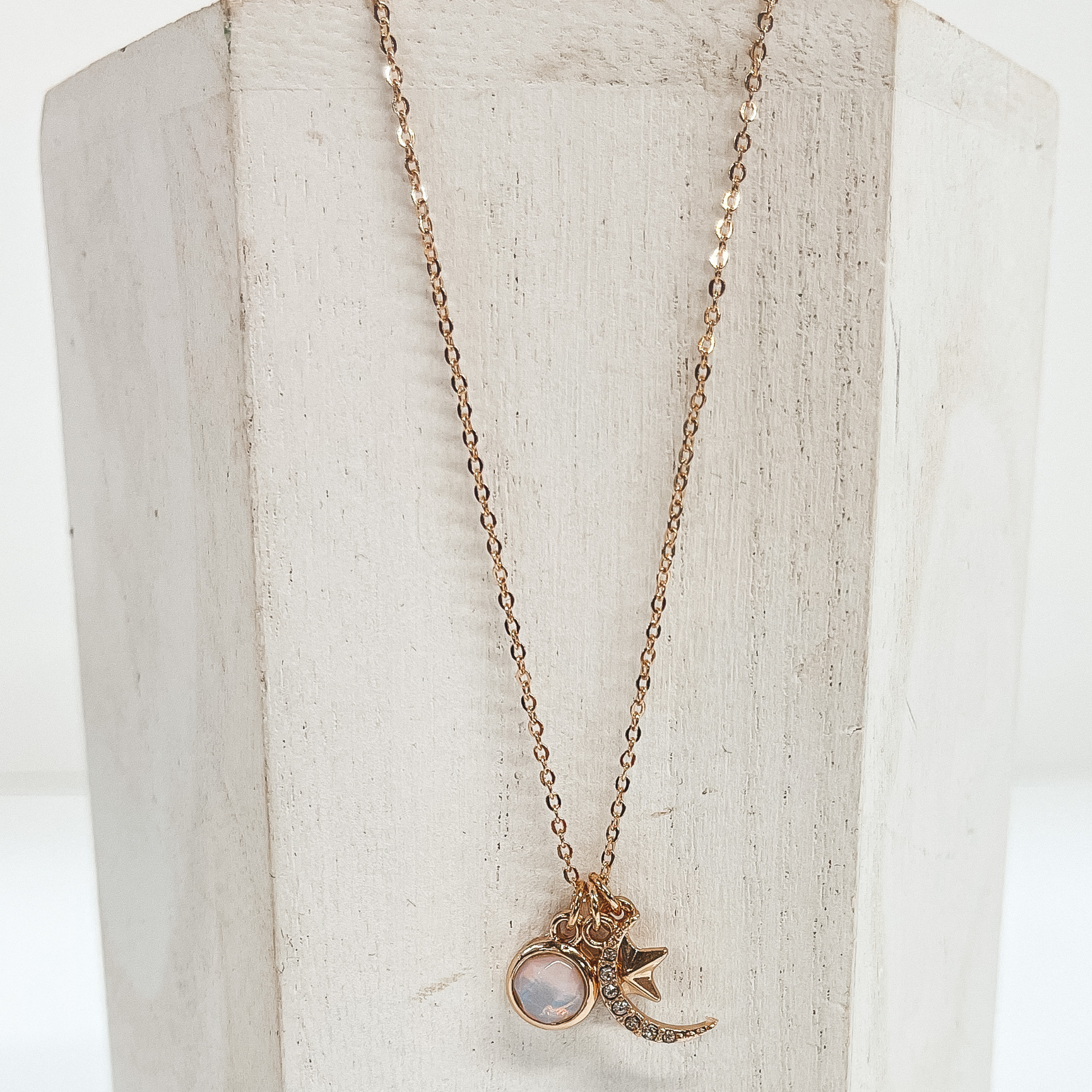 This is a thin gold chain necklace with three kinds  of pendants. One is a circle pendant with an opal  stone, a star, and a moon filled with CZ  crystals. Taken on a white block and white  background.