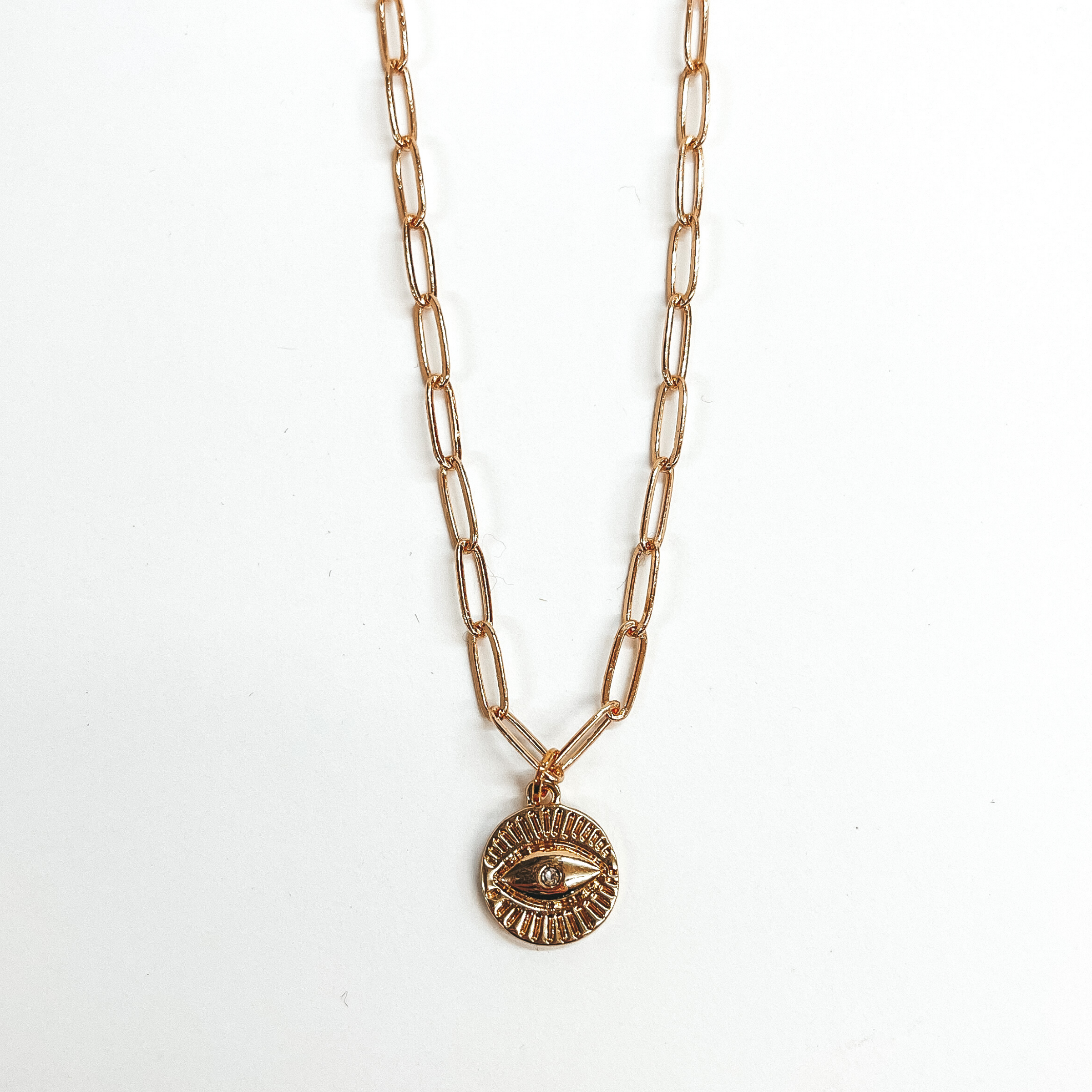 This is a gold paperclip chain necklace with a  gold evil eye pendant. This is taken on a white  background.