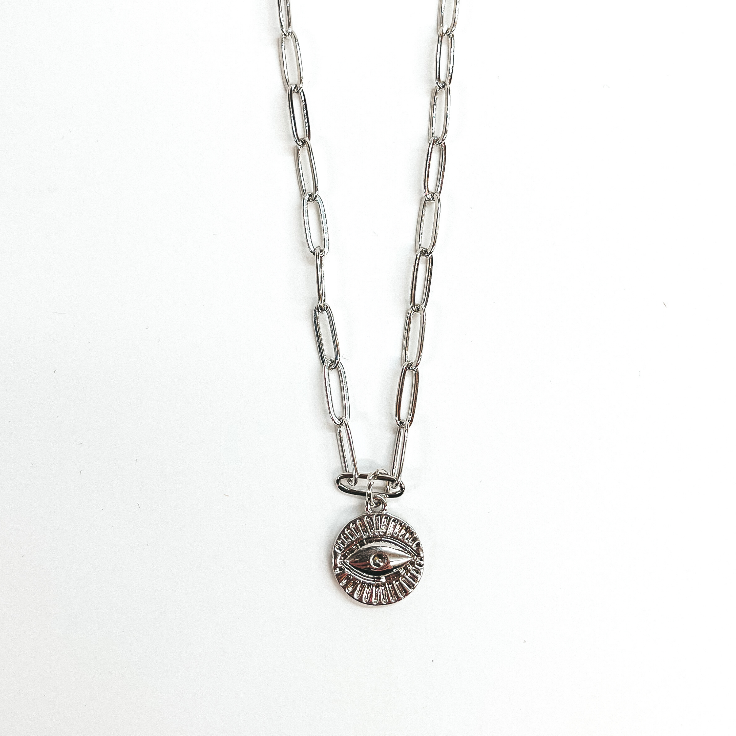 This is a silver paperclip chain necklace with a  silver evil eye pendant. This is taken on a white  background.