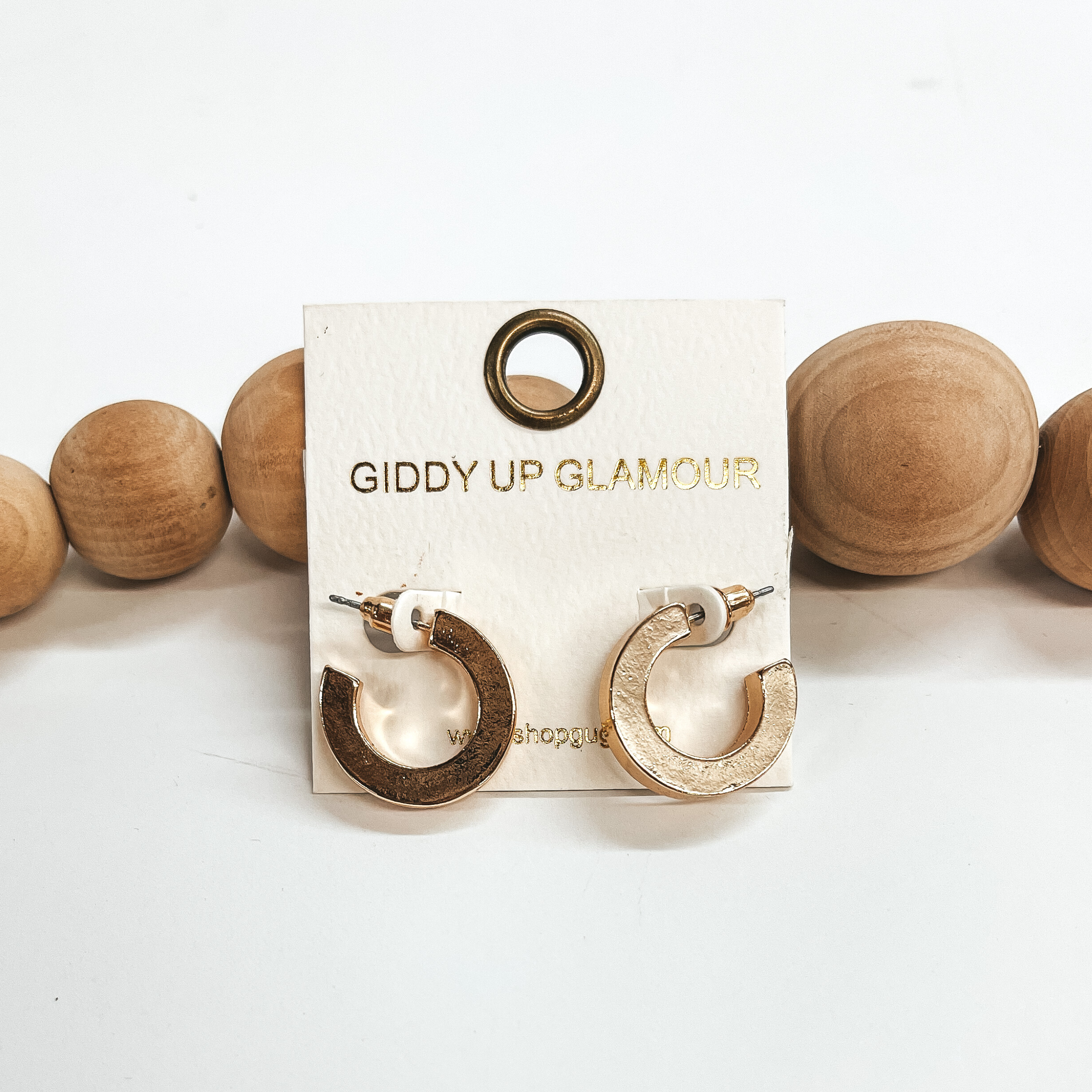 These are small shiny gold hoops with a post back  backing. Taken on a white background and leaned up  against brown wood balls.