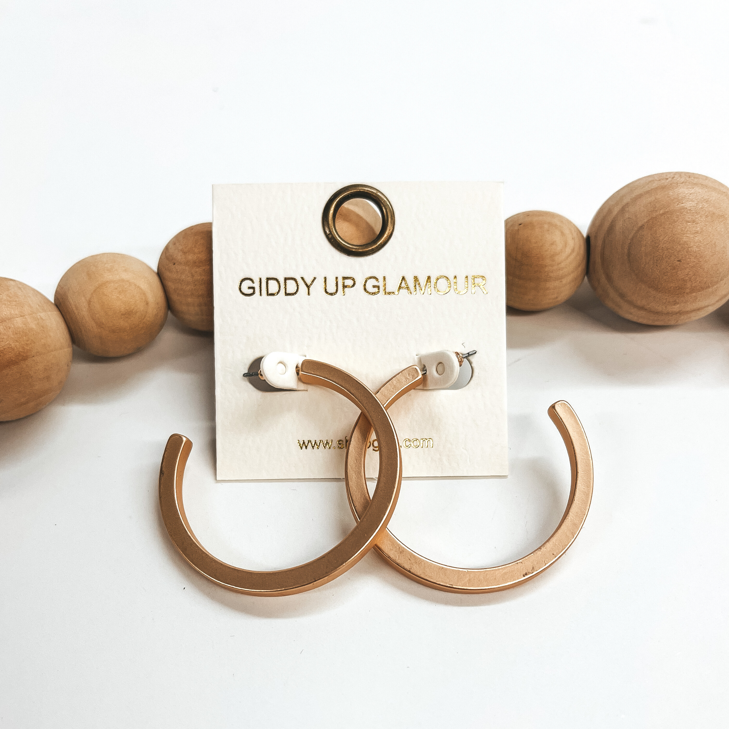 These are large matte gold hoops with a post back  backing. Taken on a white background and leaned up  against brown wood balls.