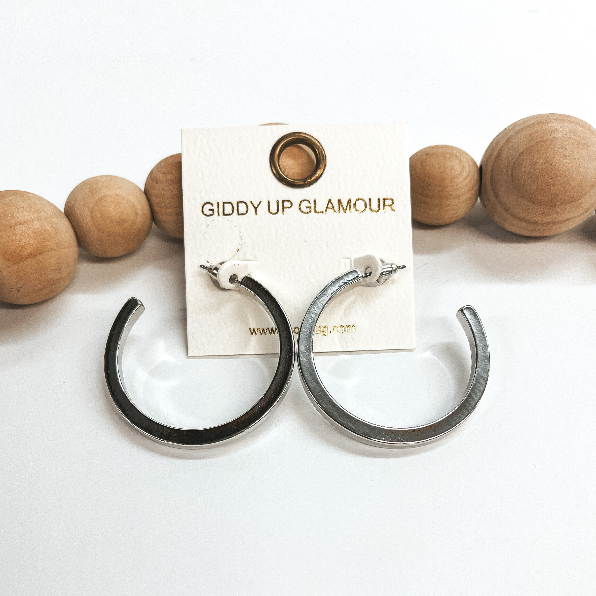 These are large shiny silver hoops with a post back  backing. Taken on a white background and leaned up  against brown wood balls.