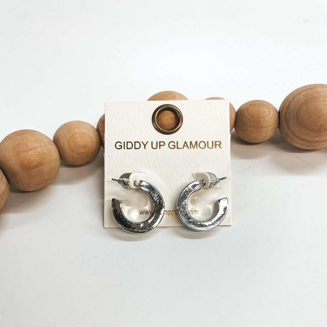 These are small shiny silver hoops with a post back  backing. Taken on a white background and leaned up  against brown wood balls.