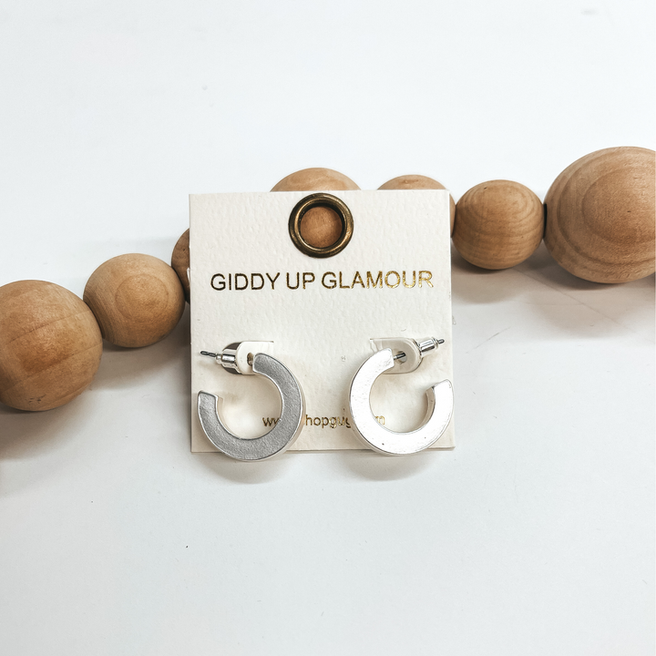 These are small matte silver hoops with a post back  backing. Taken on a white background and leaned up  against brown wood balls.