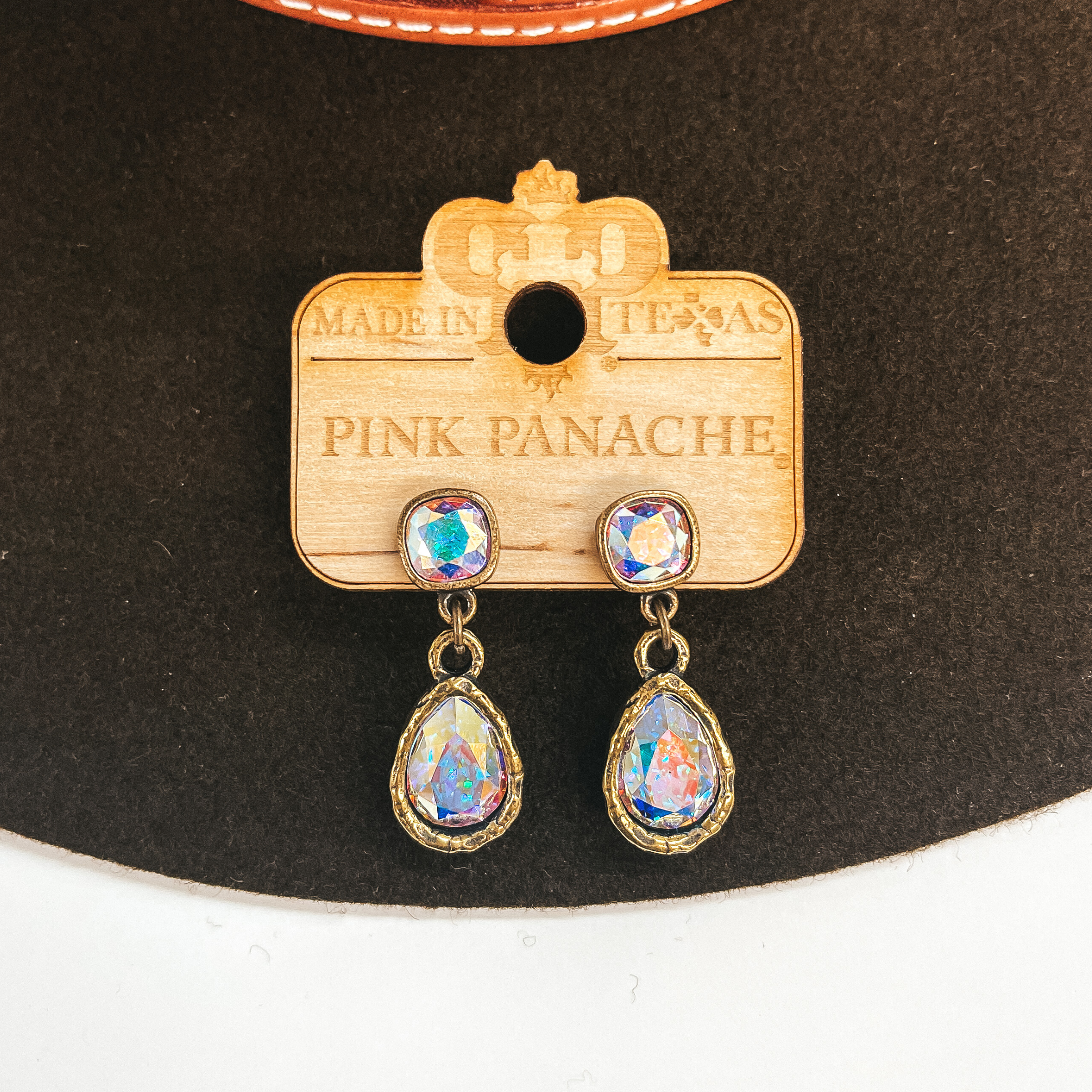 These are bronze post back earrings with an AB  cushion cut crystal connected to an AB crystal  teardrop. Taken on a dark brown hat and white  background.