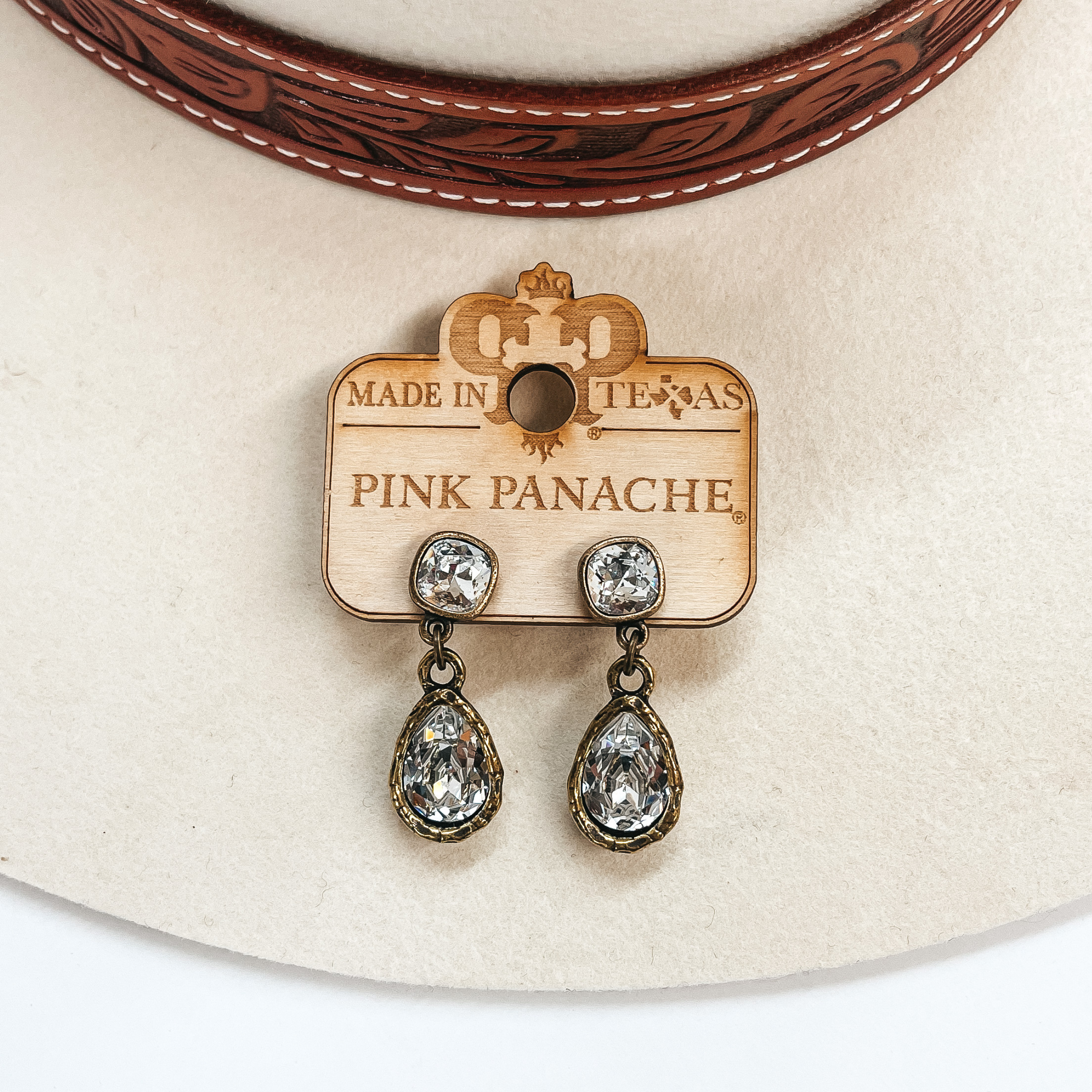 These are bronze post back earrings with a clear  cushion cut crystal connected to clear crystal  teardrop. Taken on an ivory hat and white background.