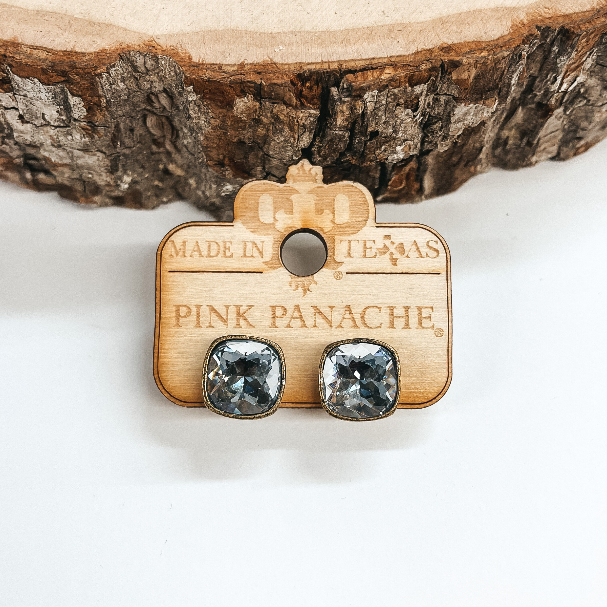 These are cushion cut crystal ignite stud earrings  in a bronze setting. These earrings are taken on a  white background and leaned up against a piece of wood. 