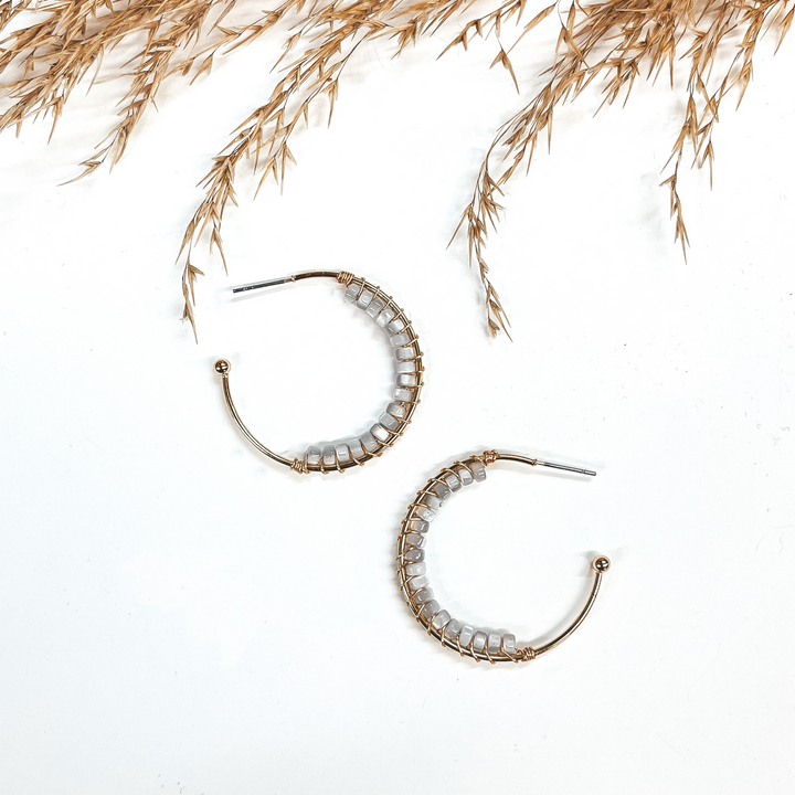 These earrings are open ended gold hoops with a post  back backing with mother of pearl beads in gray.  The beads are in the majority of the hoop with a gold  wire separating them. These earrings are taken on a  white background and brown plant in the top as decor.