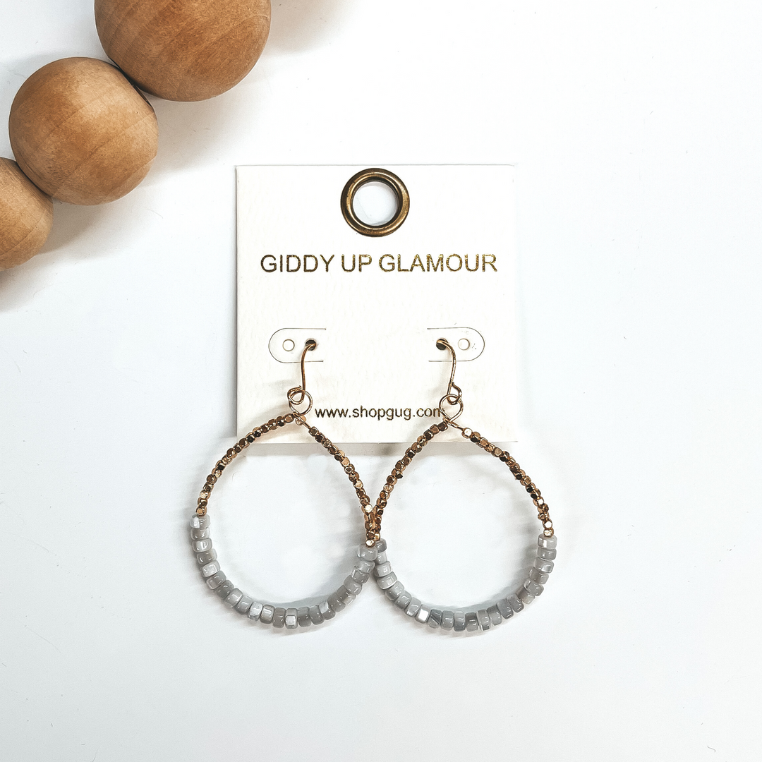 These are teardrop earrings with a fish hook backing. Bottom half has mother of pearl beads in gray  with small gold square beads in the top. These  earrings are taken on a white background and brown  wooded beads in the corner as decor.