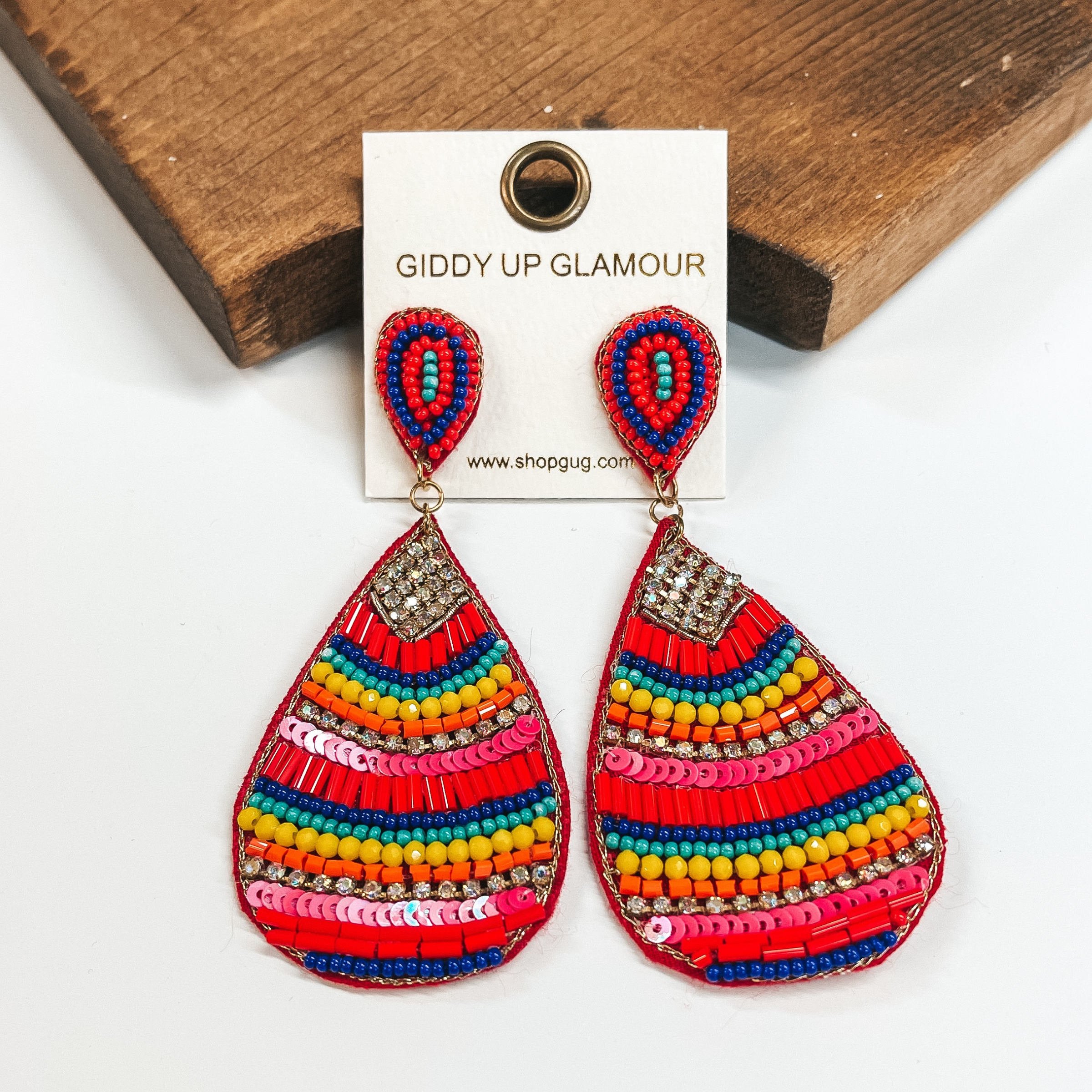These are multicolored teardrop earrings with a mix  of beads and crystals. There is a mix of different  sizes and colors of beads such as orange, red, blue,  yellow, pink, and turquoise. There is also sequins  and crystals. These earrings are taken on a white  background and leaned up against a brown block.