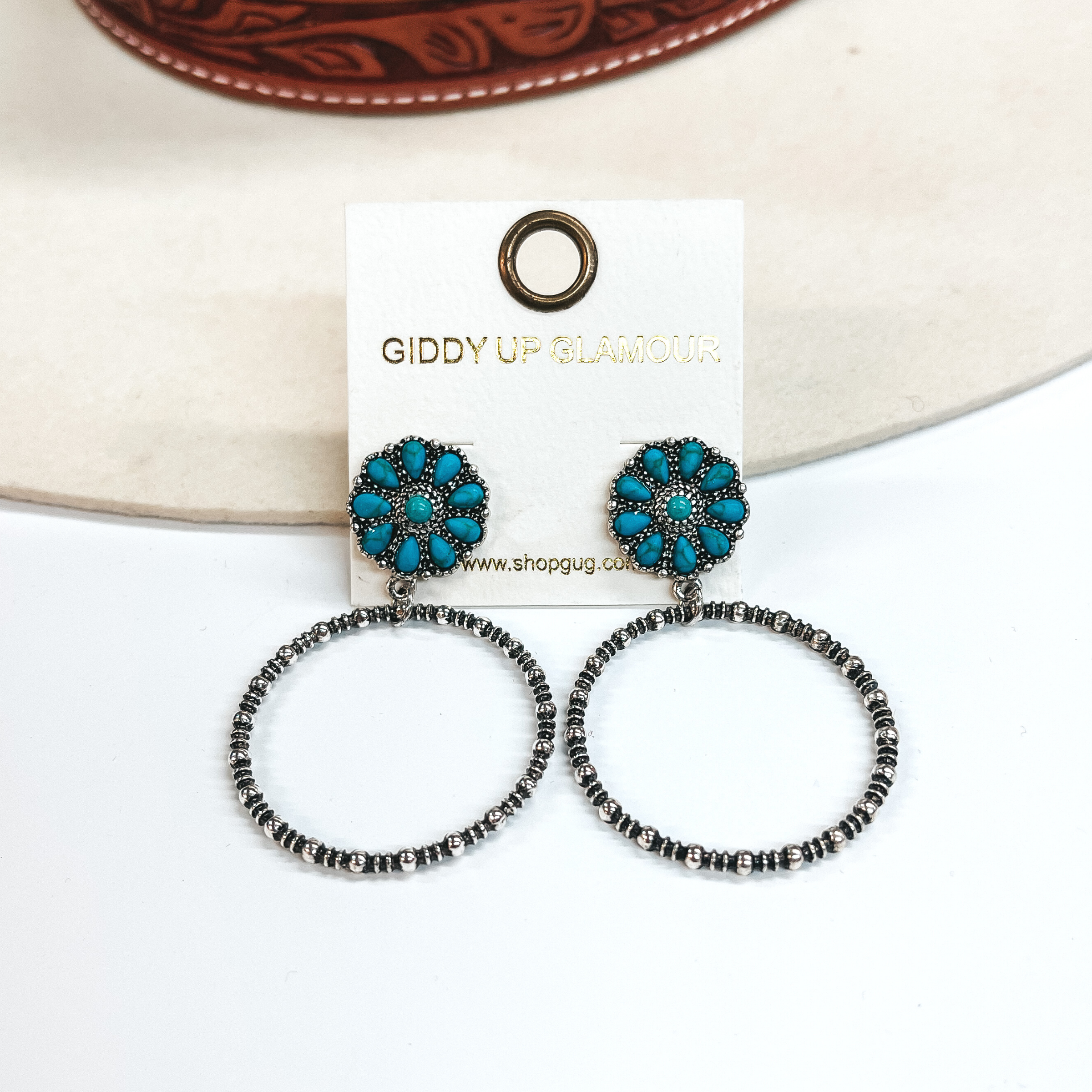 These are circle cluster post earrings with a silver  circle drop. The circle cluster has faux turquoise  stones. These earrings are taken on a white  background and leaned up against an ivory hat.