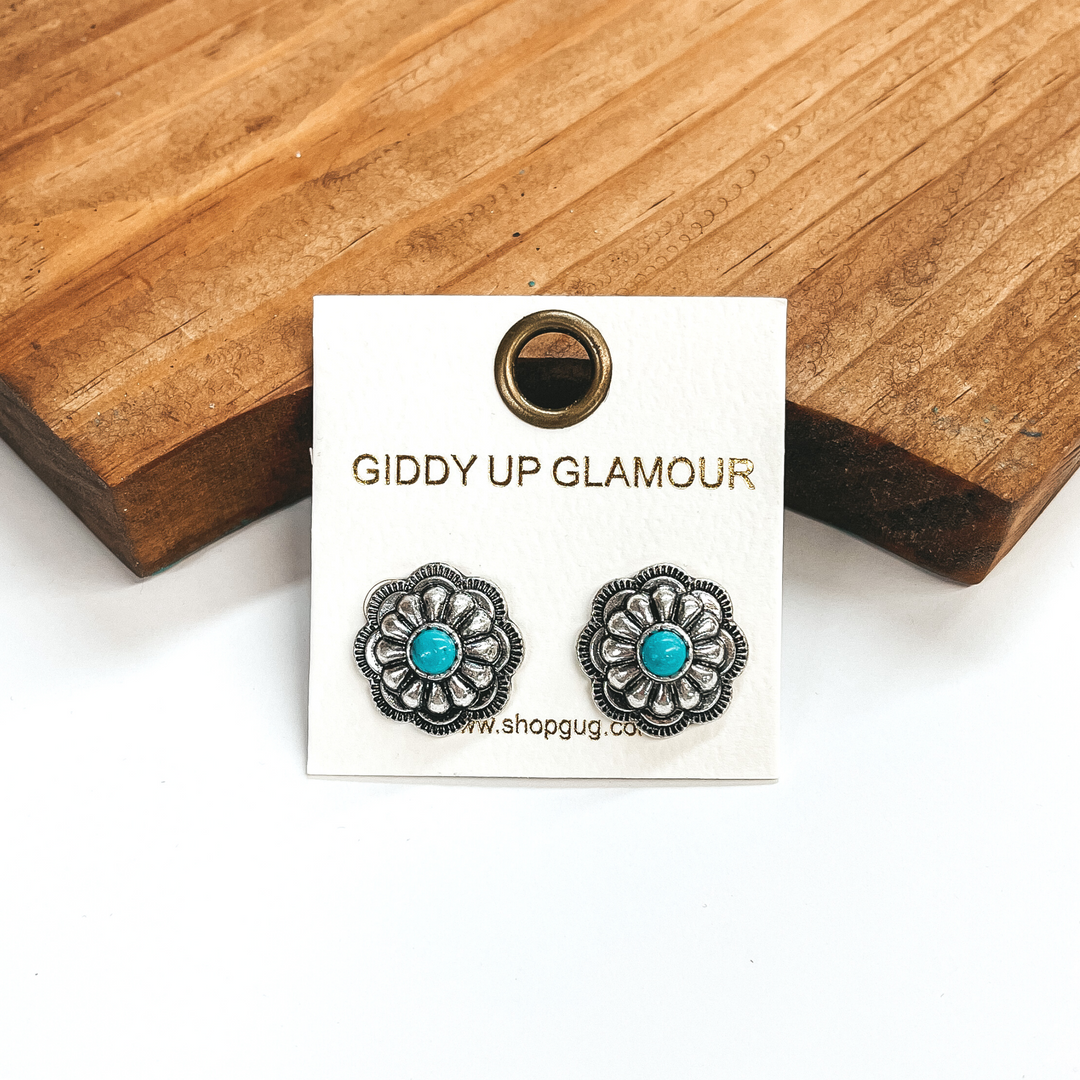 These are silver western flower post earrings with  faux turquoise stones in the center. These earrings  are taken on a white background and leaned up  against a brown block.