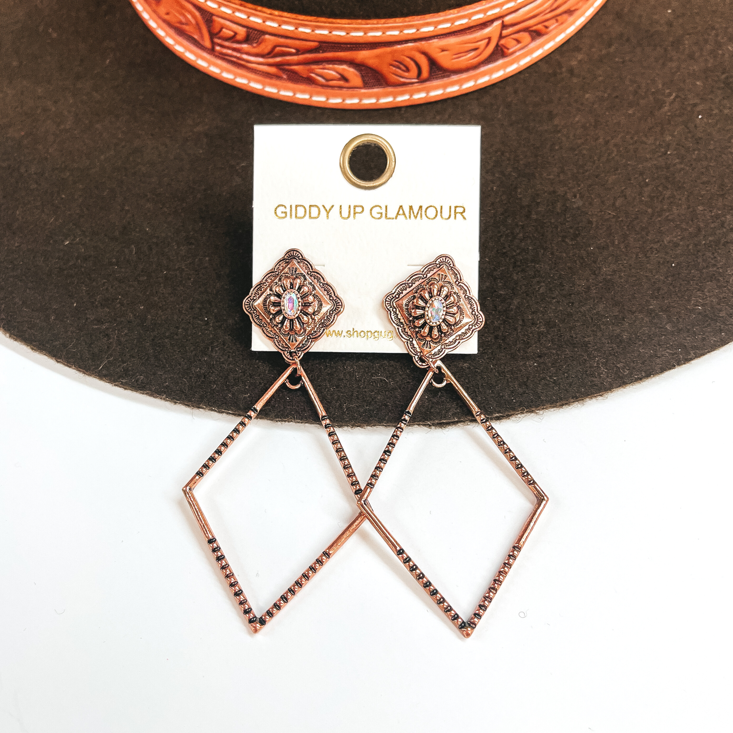 These are copper diamond shaped post back earrings  with an AB crystal in the center. It has a  diamond drop as well with textured sides. These  earrings are taken on a dark brown felt hat and a  white background.