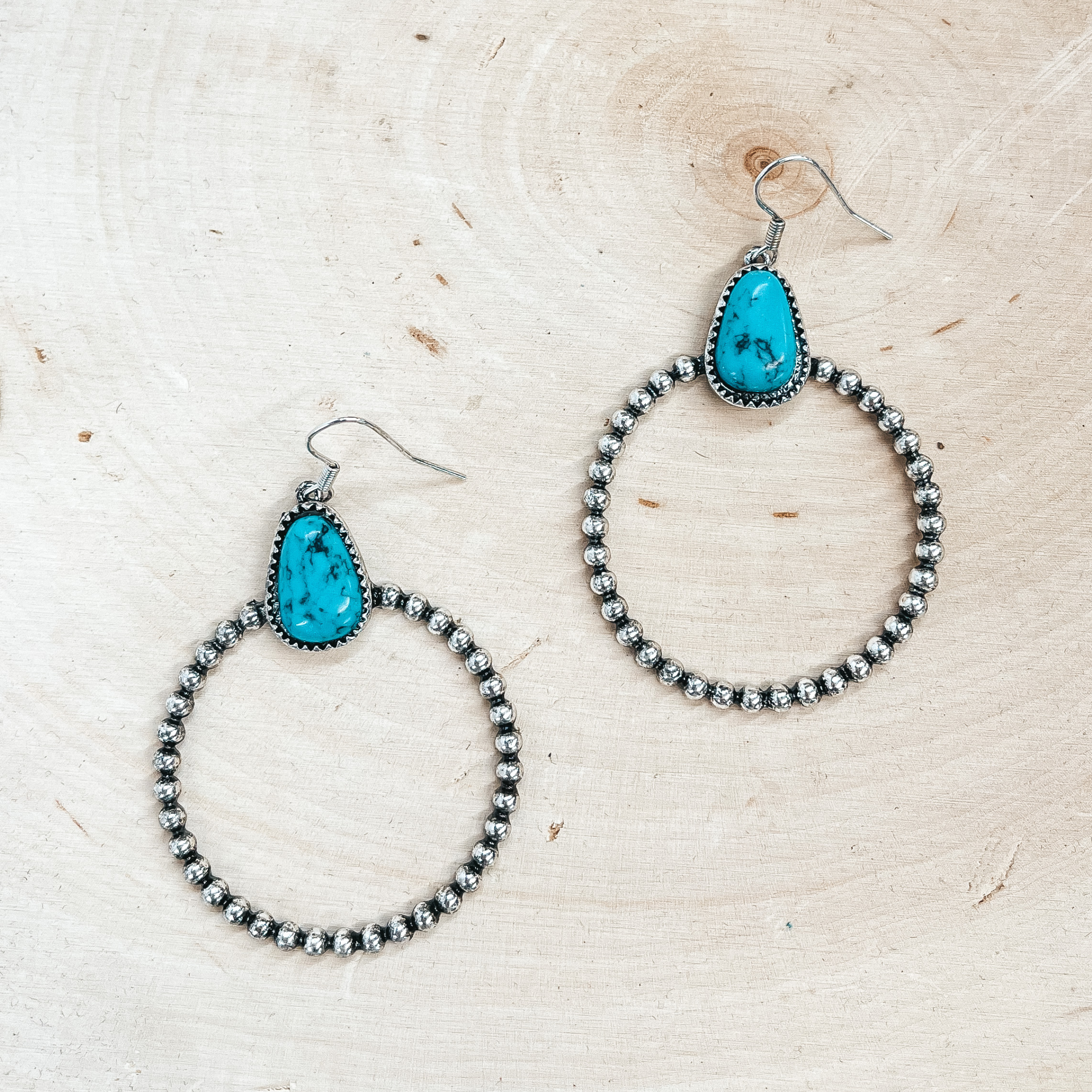 These are silver fish hook earrings with a faux  turquoise stone and a silver beaded circle drop. The circle drop has a beaded texture in the front  and a smooth back. These earrings are taken on a  slab of wood.