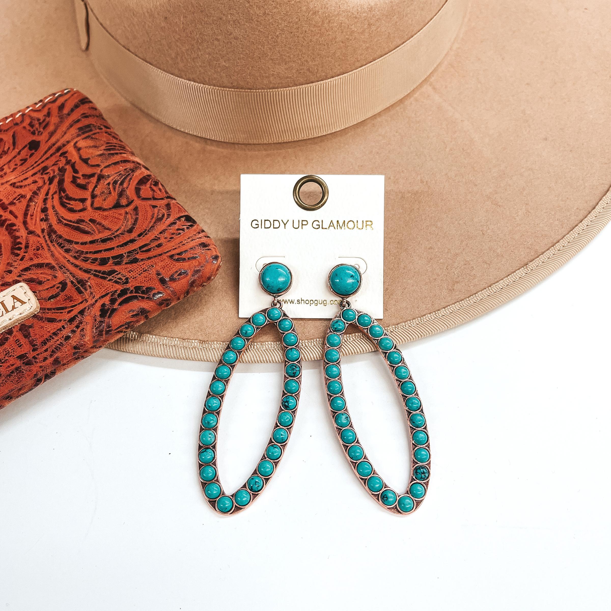 These are open oval drop earrings with turquoise  stones.  Post back earrings with a small stone and an open  oval drop with turquoise stones all around in a  copper setting.  These are  taken on a light brown hat brim and white background.  There is a leather printed wallet in the side  as decor.