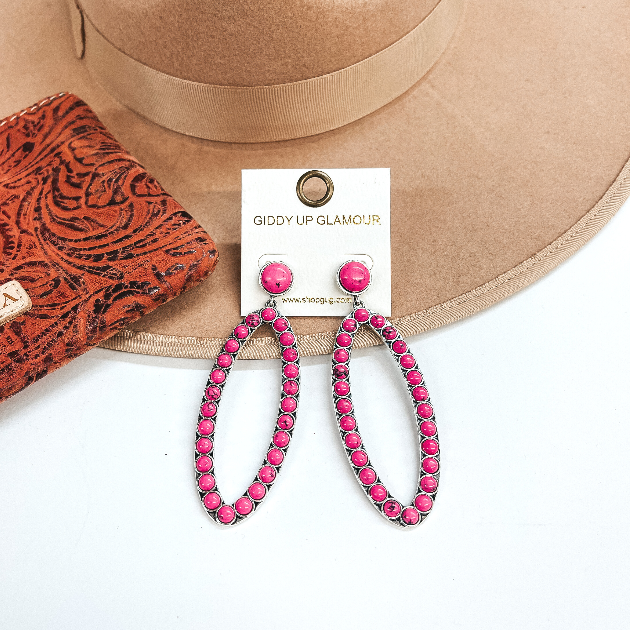 These are open oval drop earrings with pink stones.  Post back earrings with a small stone and an open  oval drop with pink stones all around. These are  taken on a light brown hat brim and white background.  There is a leather printed wallet in the side  as decor.