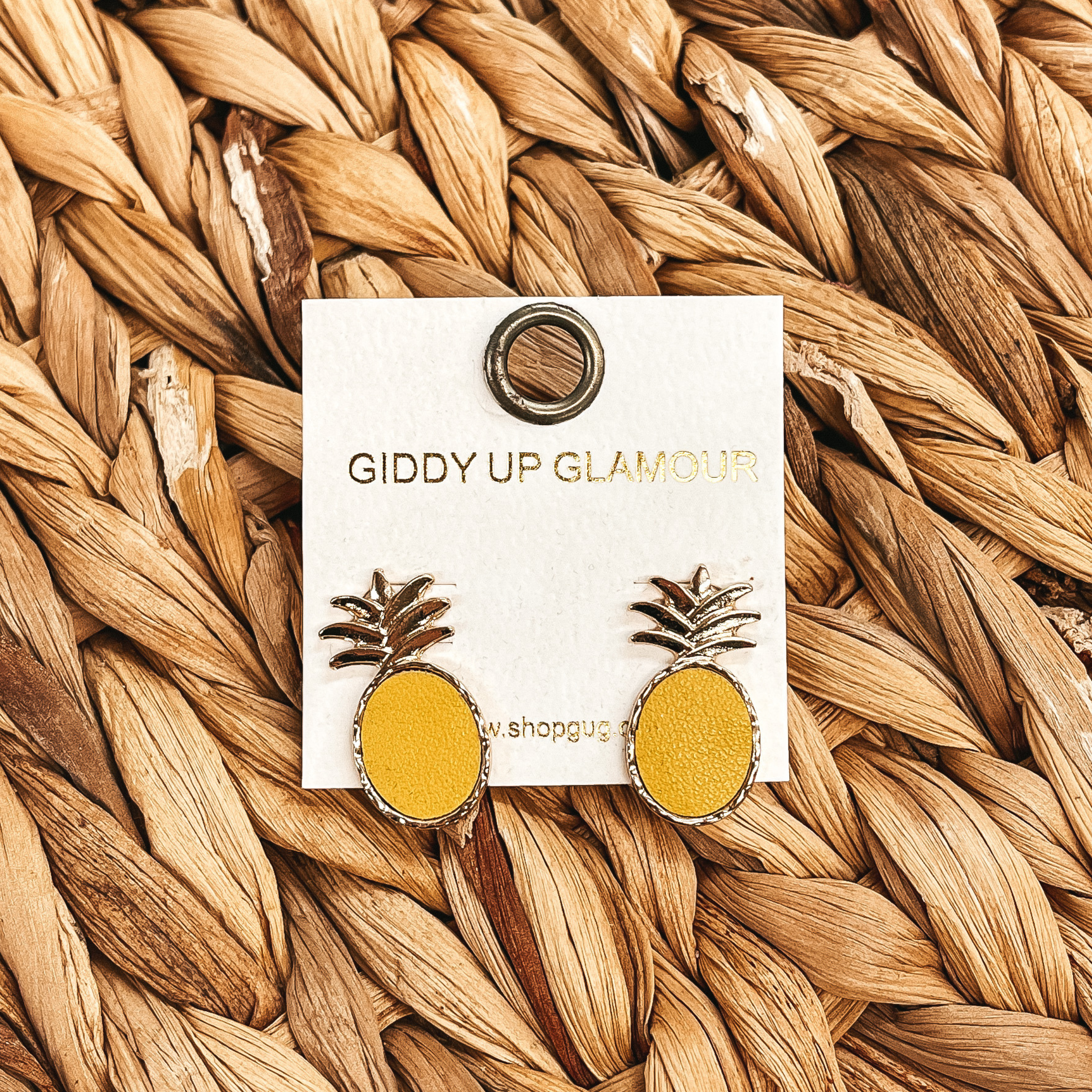These are gold and yellow pineapple post back  earrings, the yellow is faux leather and it's in  a gold setting. These earrings are taken on a brown  woven plate.