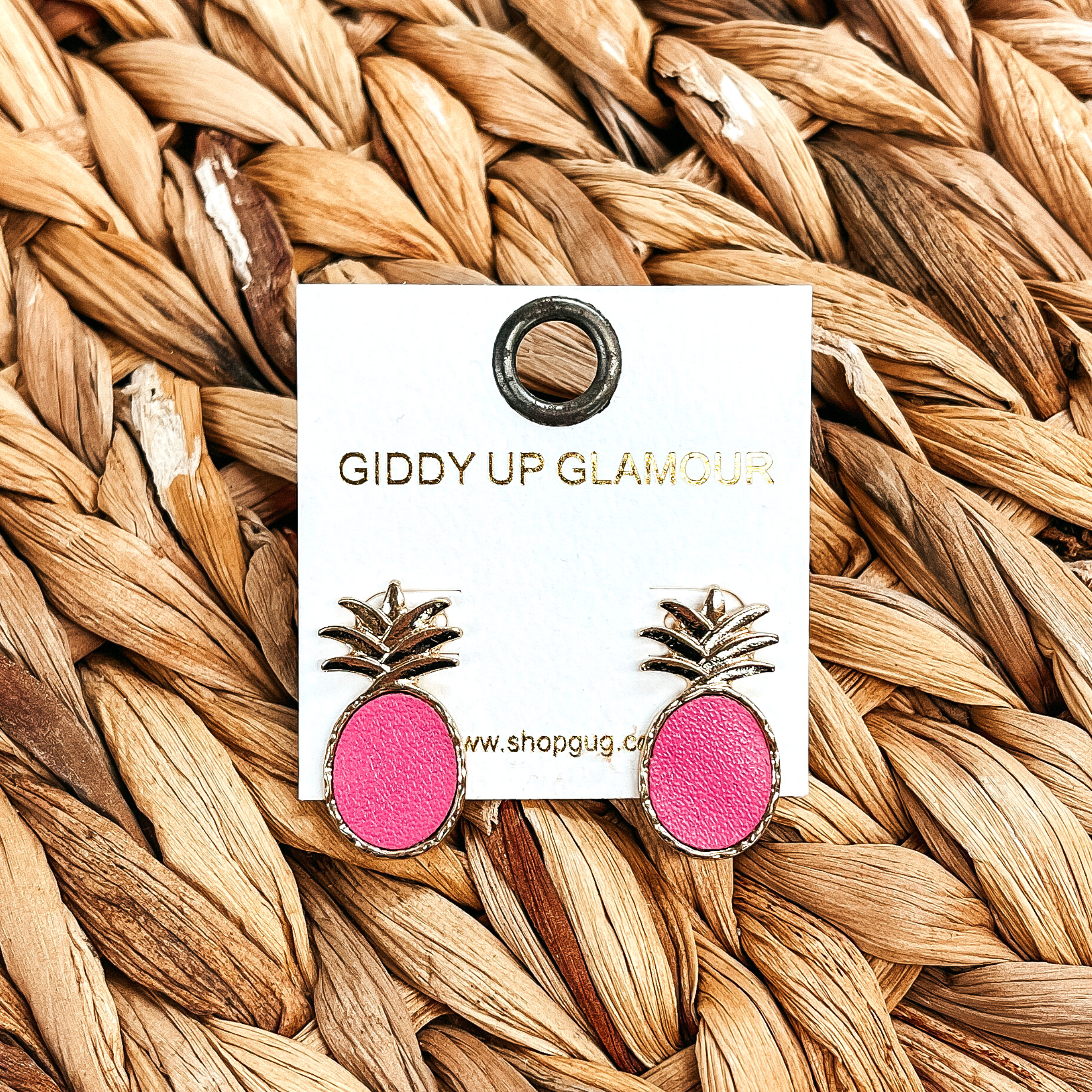 These are gold and pink pineapple post back  earrings, the pink is faux leather and it's in  a gold setting. These earrings are taken on a brown  woven plate.