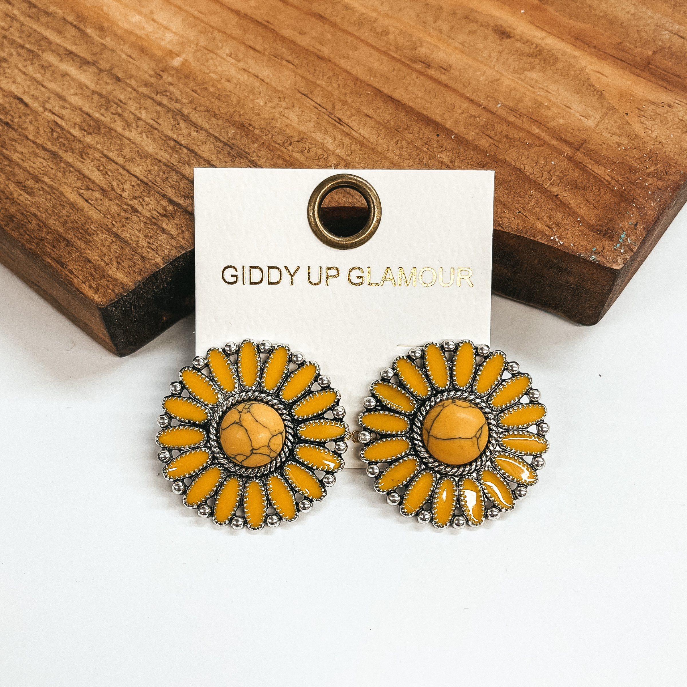 Yellow concho earrings with a center yellow stone  and silver outline. These earrings are pictured  leaning up against a brown block with a white  background.