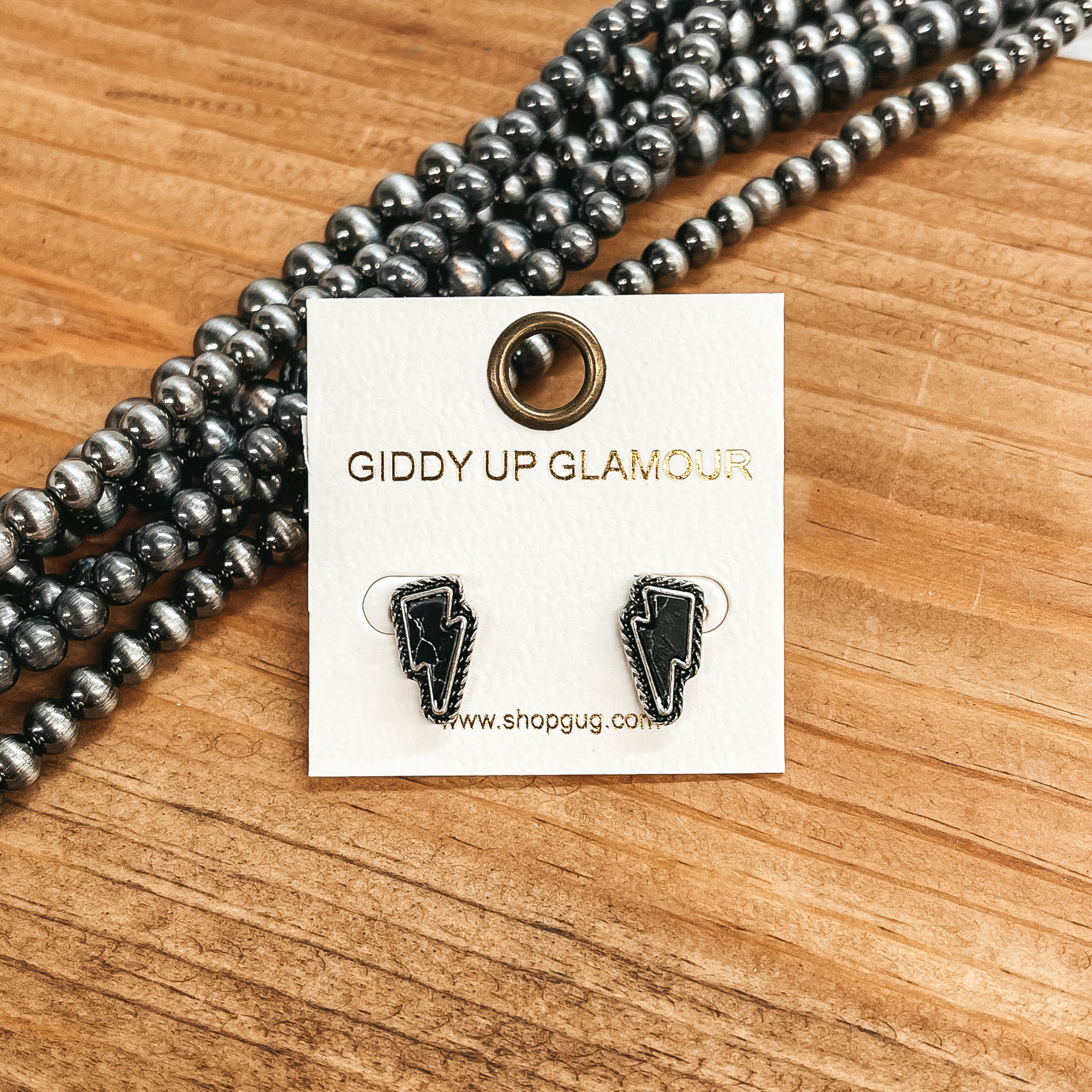 These are small lightning bolt faux black  stone in a silver setting with detailing. These  earrings are taken on a brown block with Navajo  pearls in the side as decor.