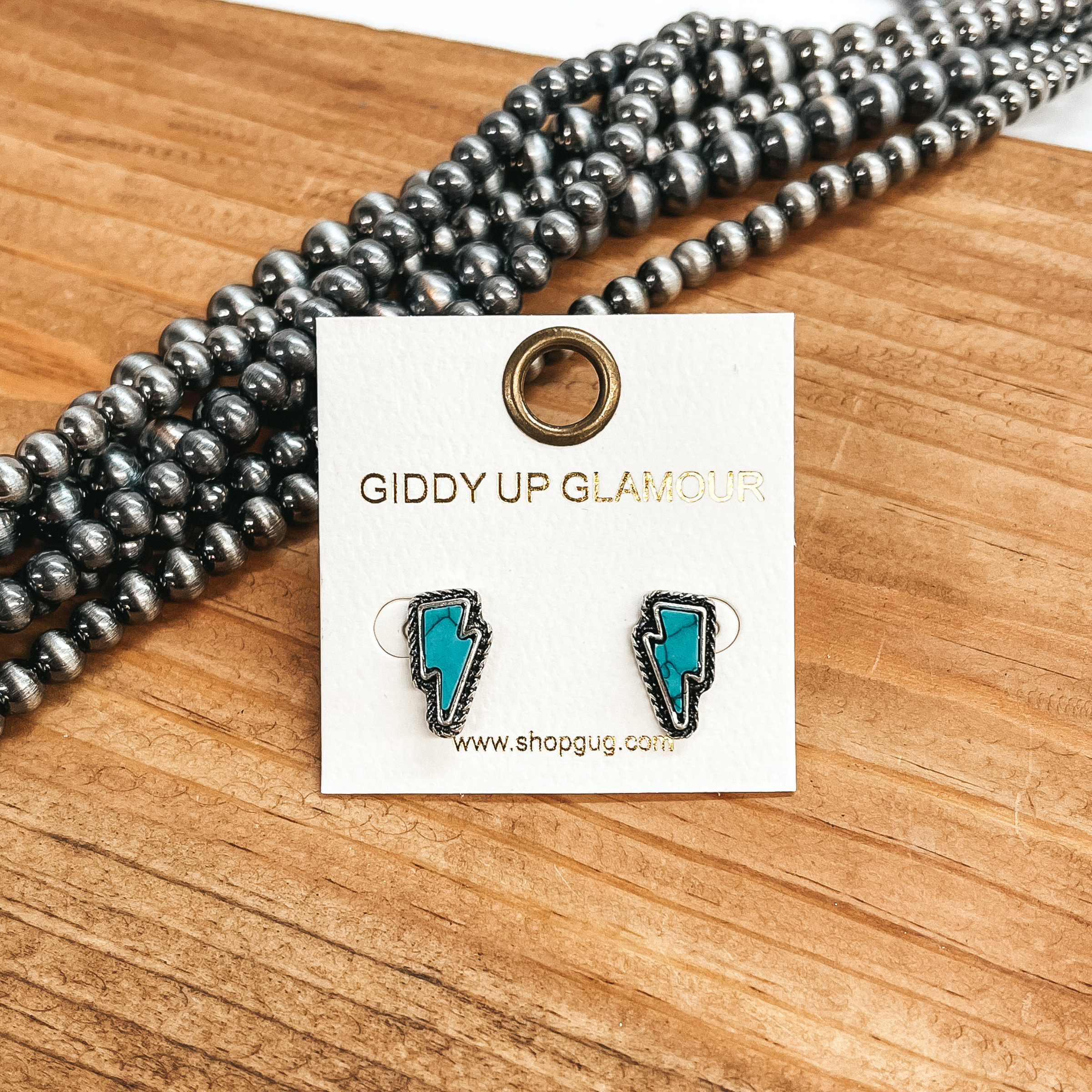 These are small lightning bolt faux turquoise  stone in a silver setting with detailing. These  earrings are taken on a brown block with Navajo  pearls in the side as decor.