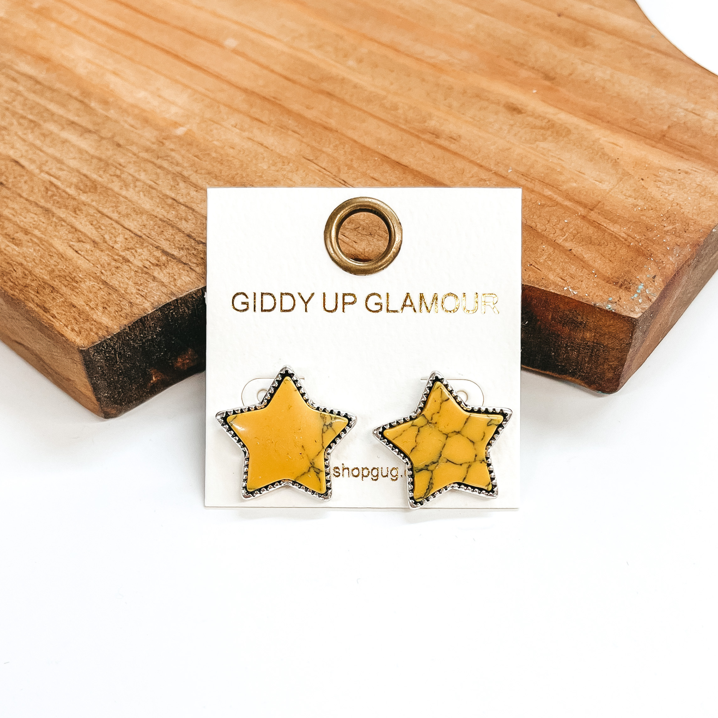 These are yellow faux stone star shaped post back  earrings in a silver setting. These earrings are  taken leaning against a brown block and a white  background.