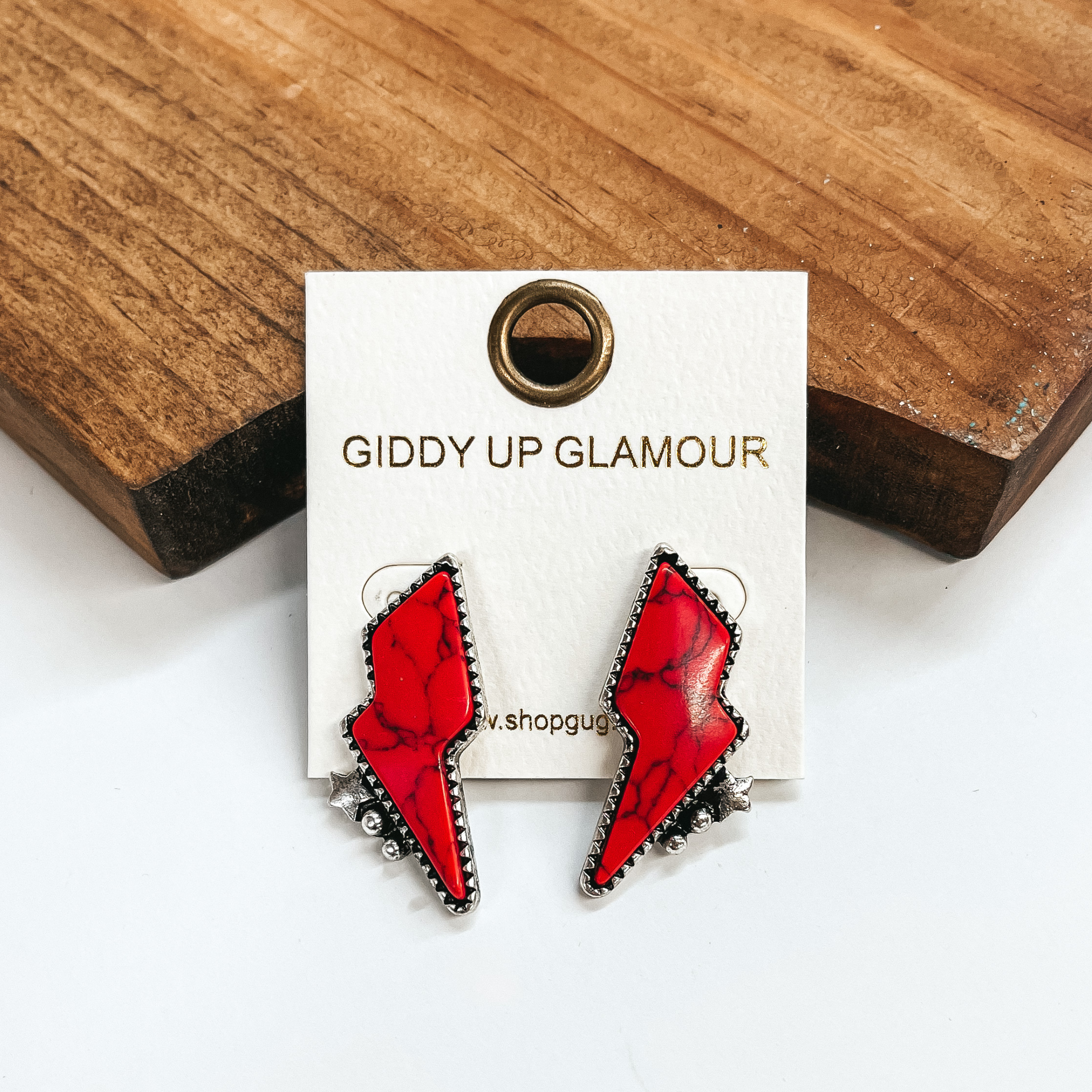 These are red faux stone lightning bolt  post back earrings in a silver setting, they also  have detailing in the bottom; a small star and two  circles. These earrings are taken on leaning up  against a brown block and a white background.