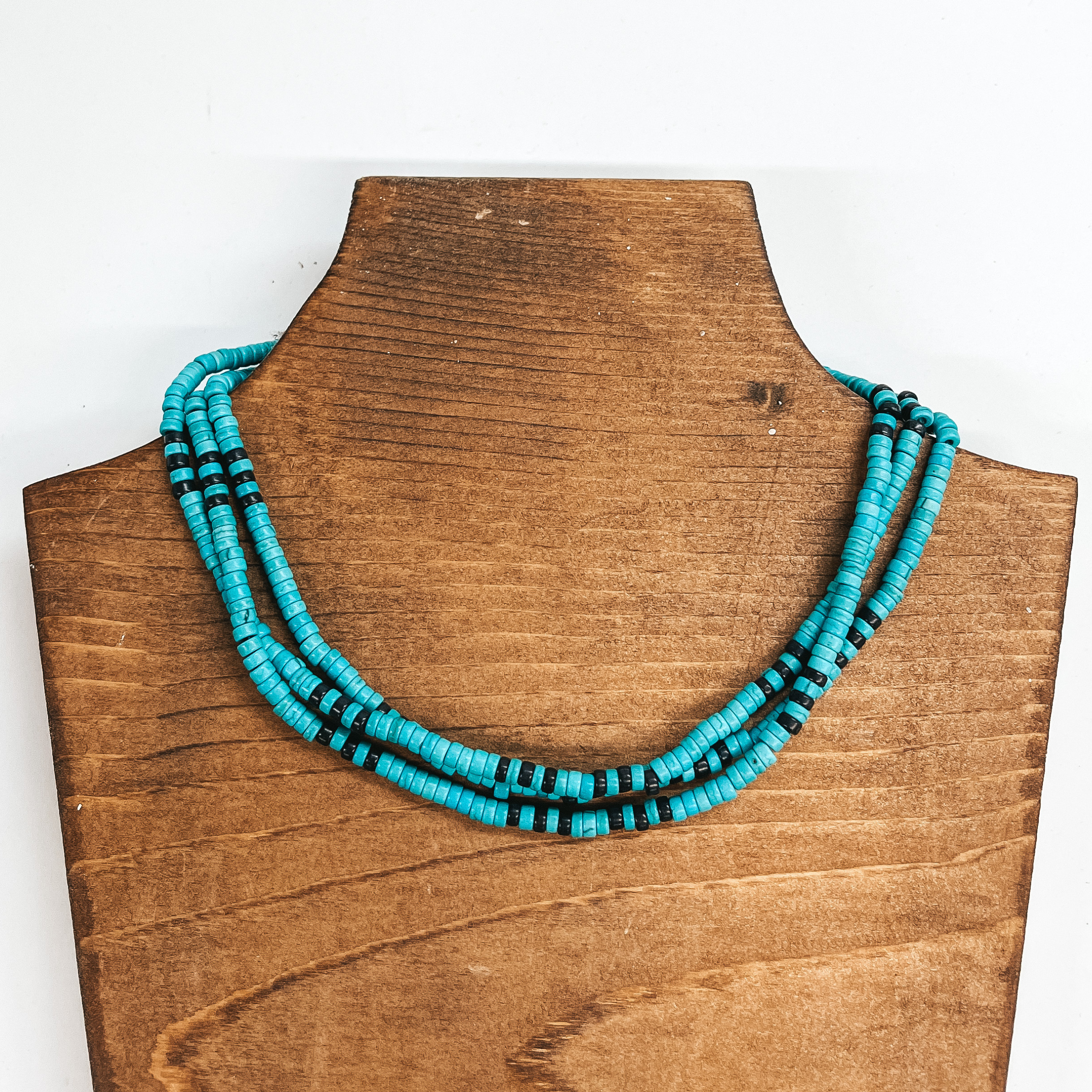 Three strand beaded choker necklace with turquoise  and black beads. The necklace is taken on a brown  block and a white background.