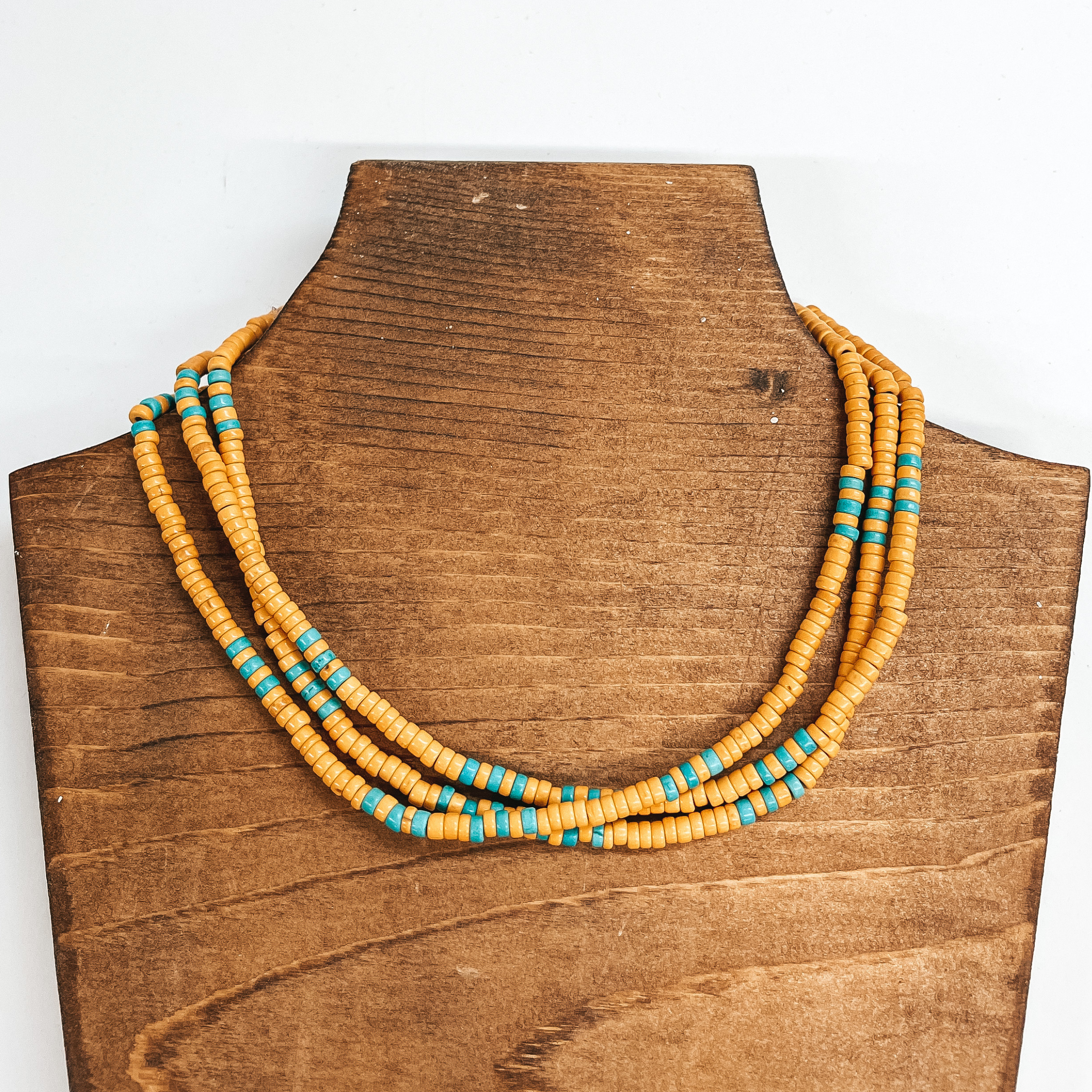 Three strand beaded choker necklace with yellow  and turquoise beads. The necklace is taken on a  brown block and a white background.
