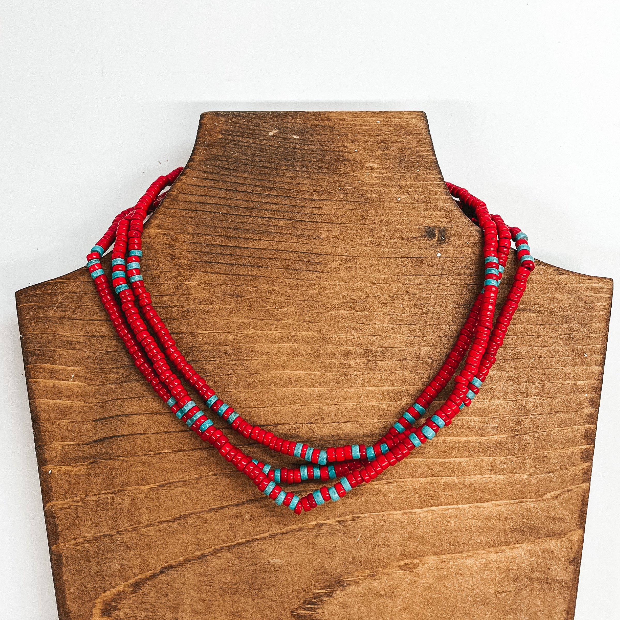 Three strand beaded choker necklace with red  and turquoise beads. The necklace is taken on a  brown block and a white background.