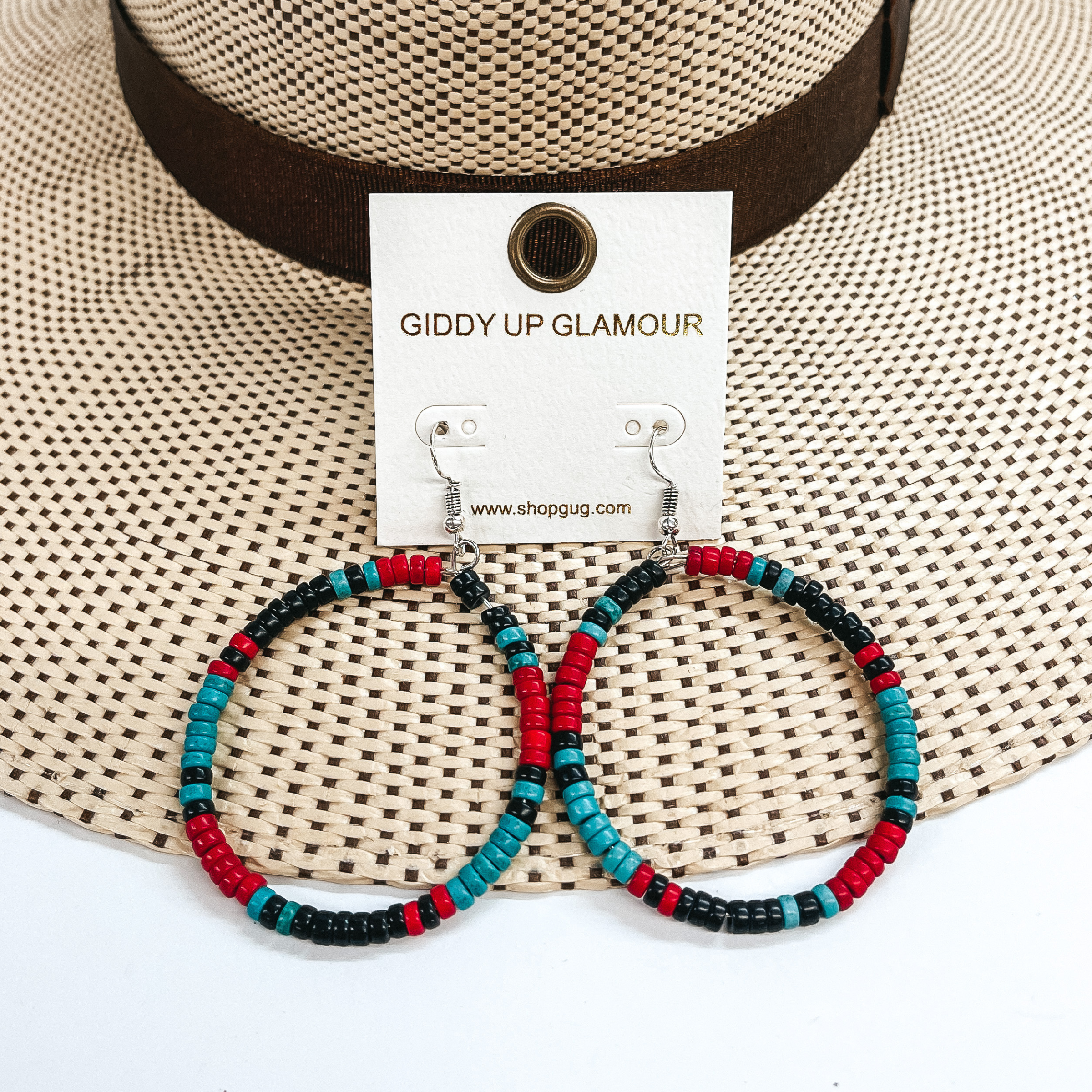 These are circle hoop earrings with multicolored  beads  all around. The beads are red, turquoise, and  black. These earrings are taken on a straw hat brim  and a white background.