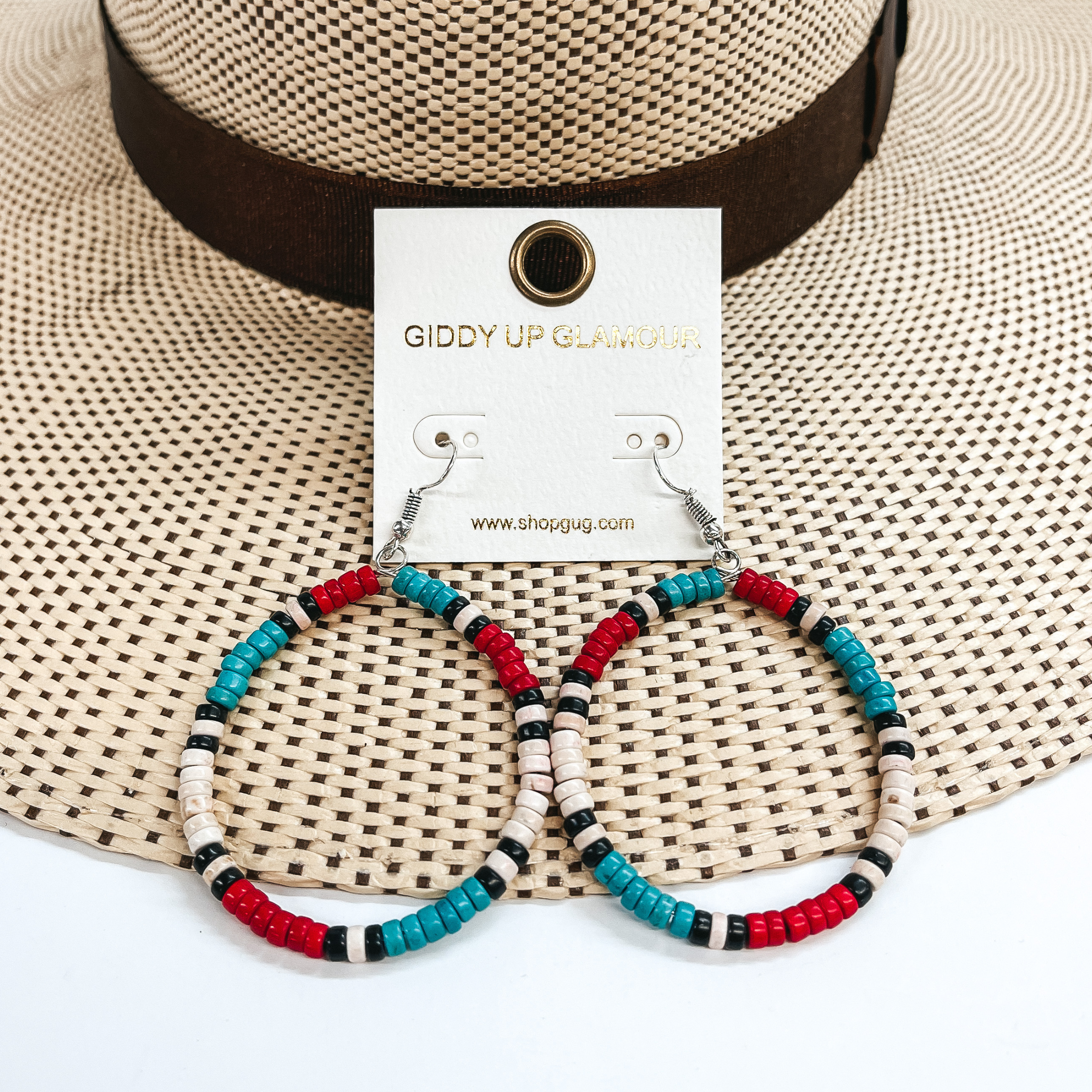 These are circle hoop earrings with multicolored  beads  all around. The beads are red, turquoise, ivory and  black. These earrings are taken on a straw hat brim  and a white background.
